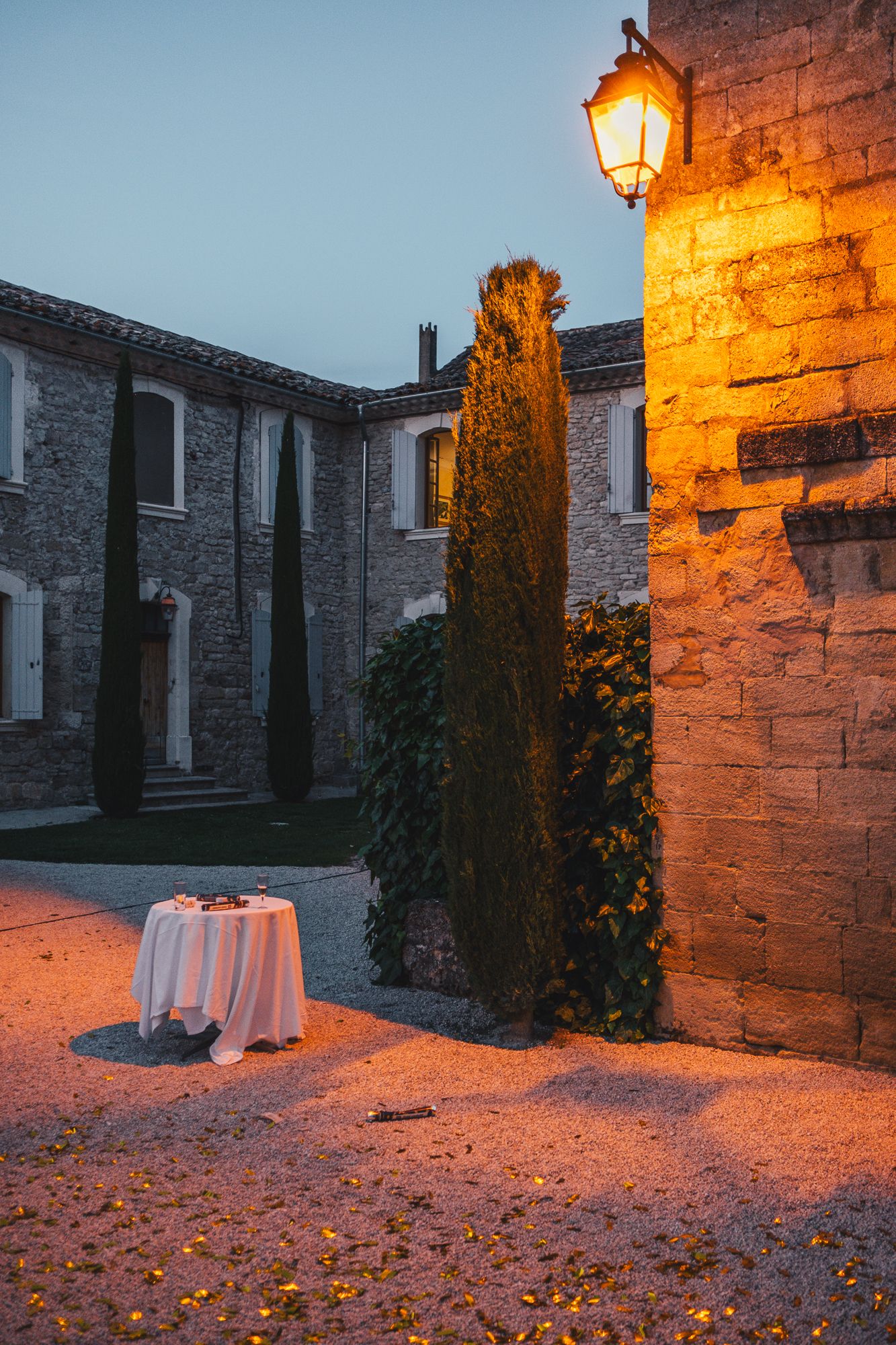 Romantic twilight wedding venue courtyard with glowing lantern illuminating stone building and white draped table.