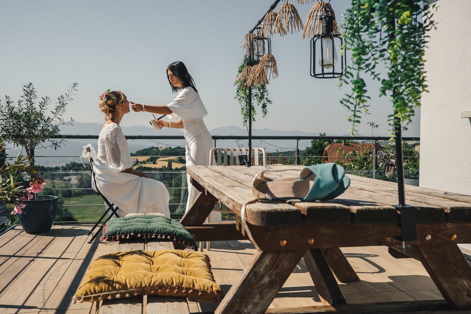 Woman receiving outdoor massage on sunny terrace with wooden furniture and lush garden views.