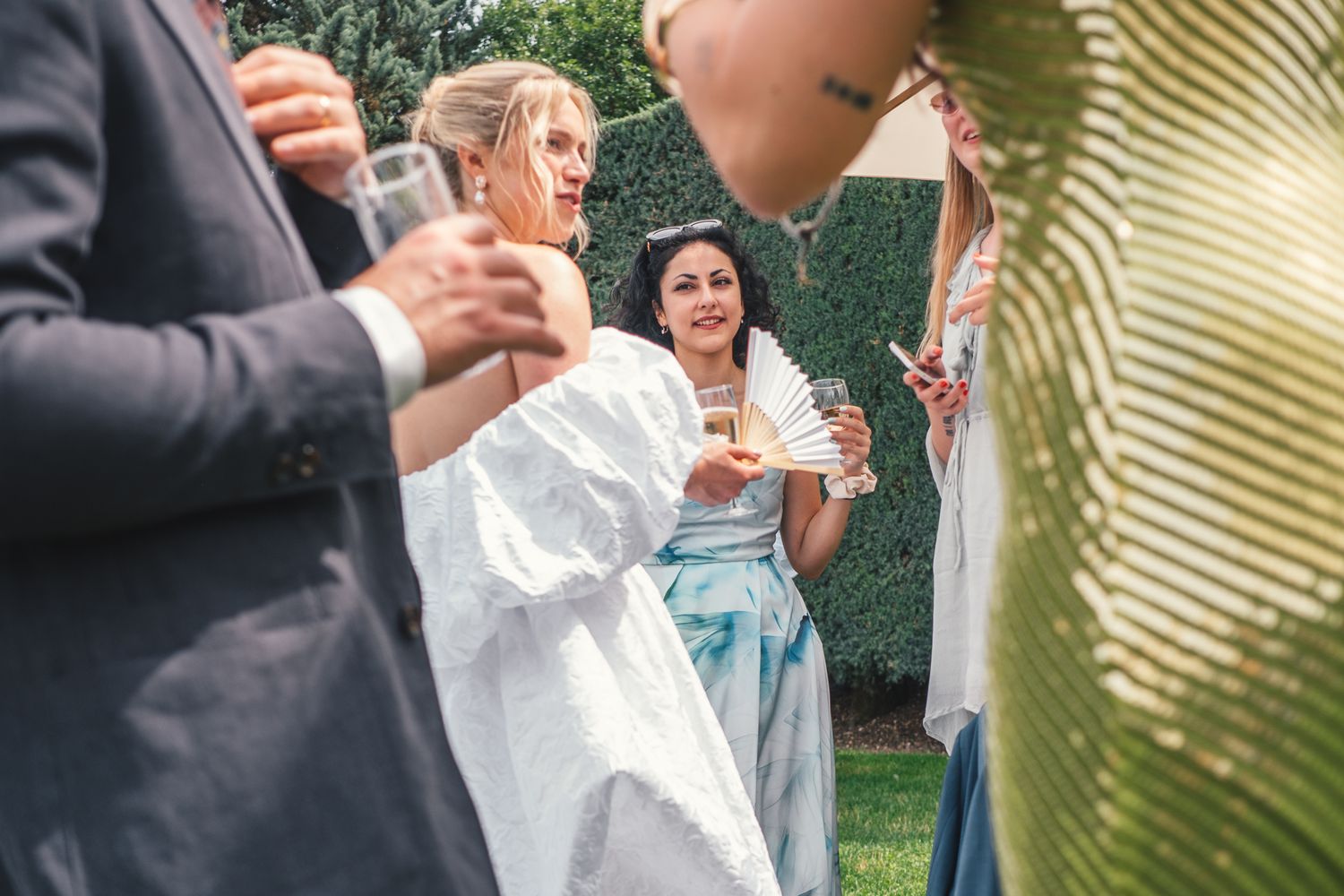 Guests socializing outdoors at a garden party, holding drinks and smiling in elegant attire.