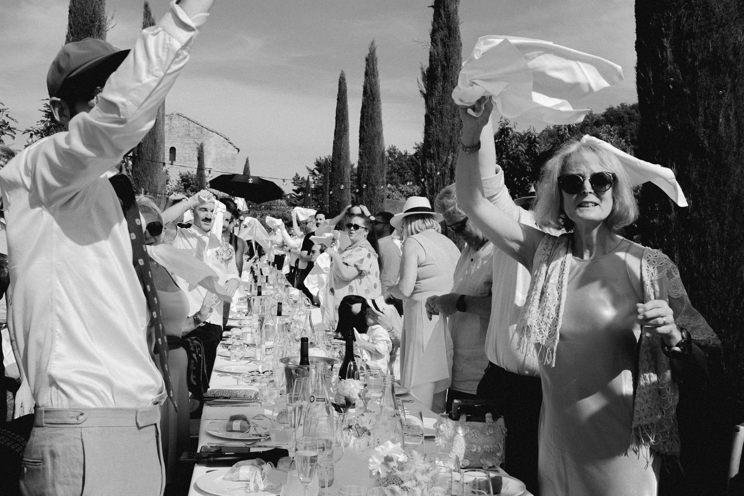Black and white photo of elegantly dressed guests in white attire celebrating at an outdoor garden party.