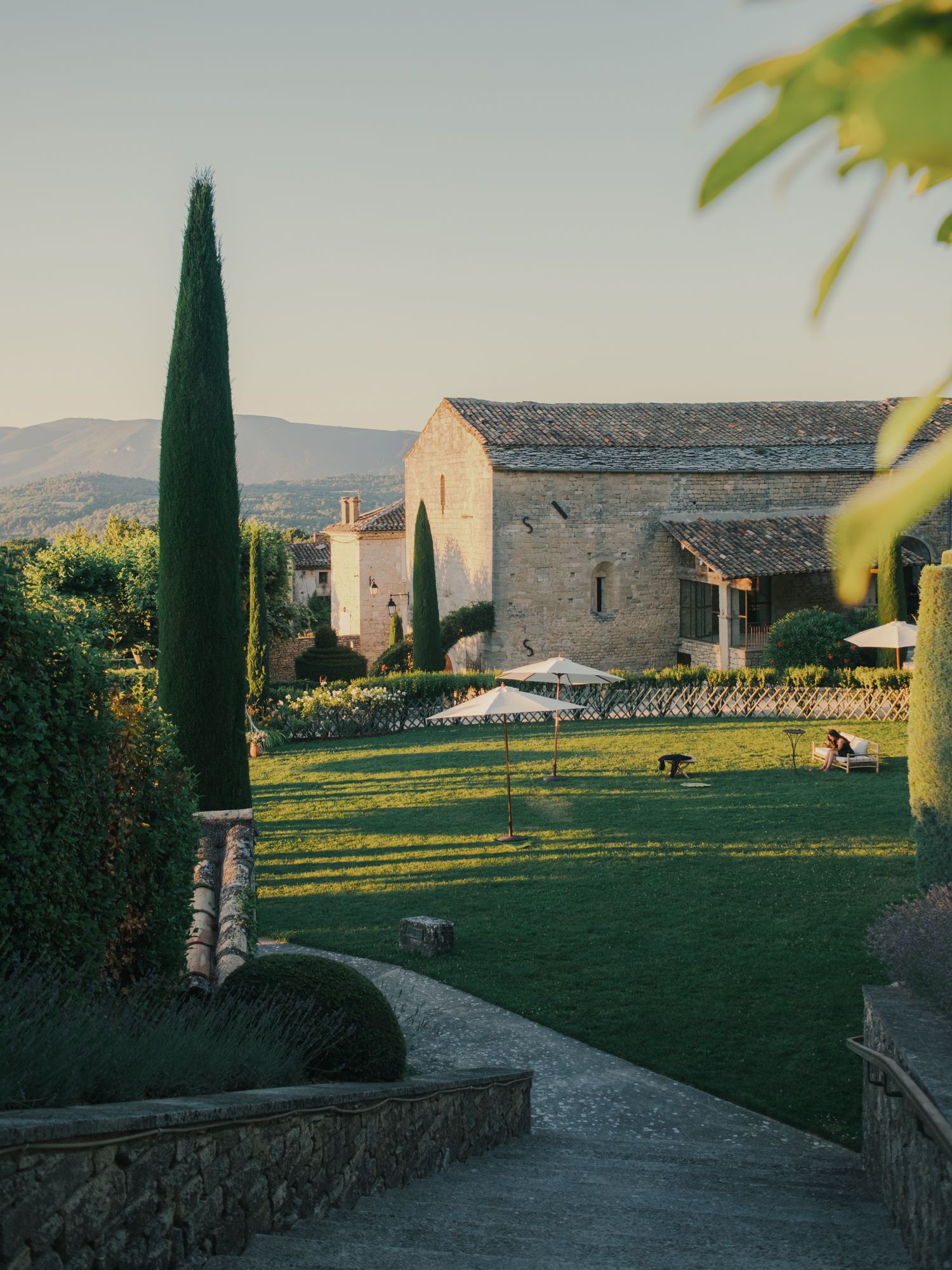 Sunlit stone farmhouse with cypress trees and manicured lawn in Provence, France.