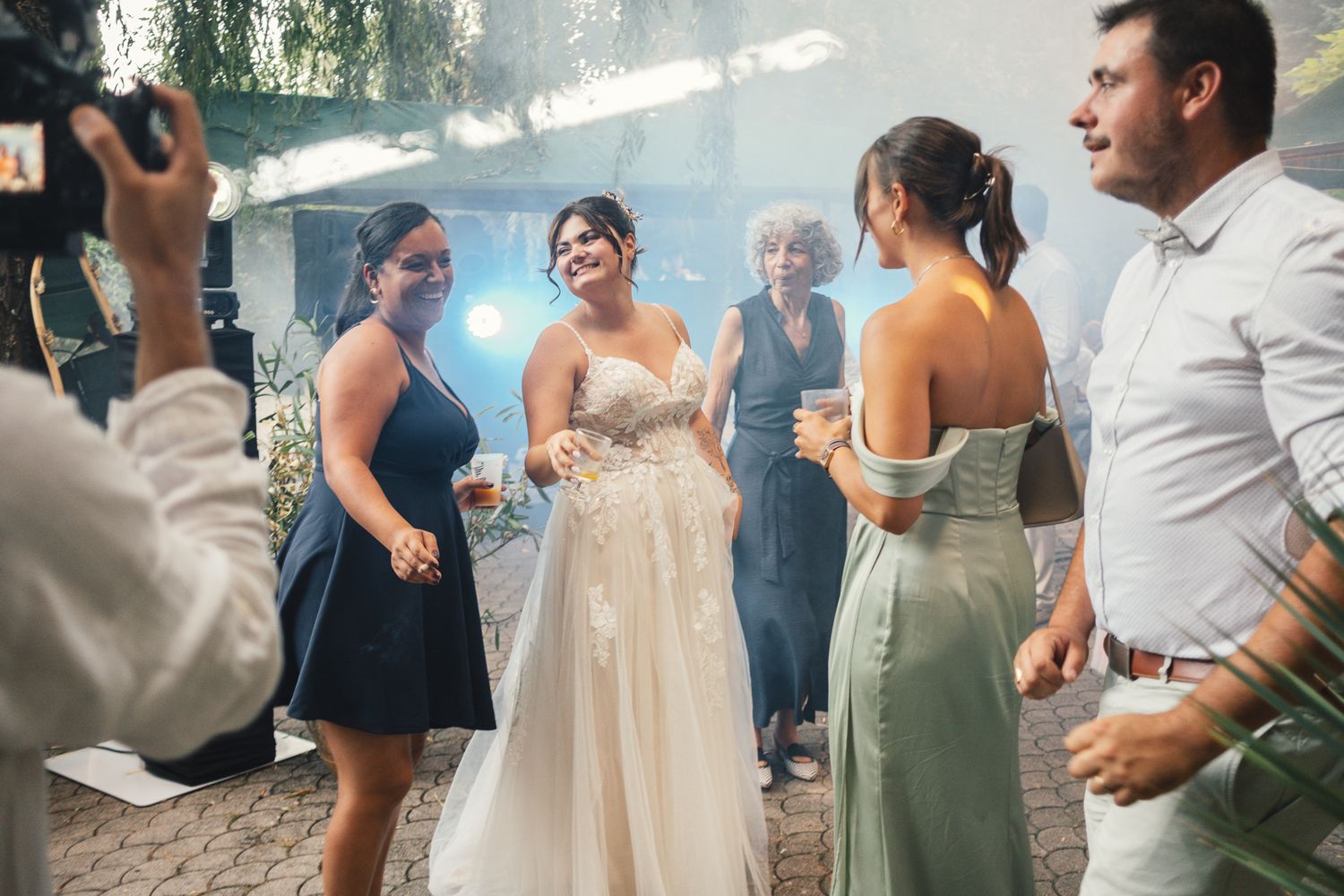 Bride in white lace gown dancing with guests at wedding reception with blue lighting.
