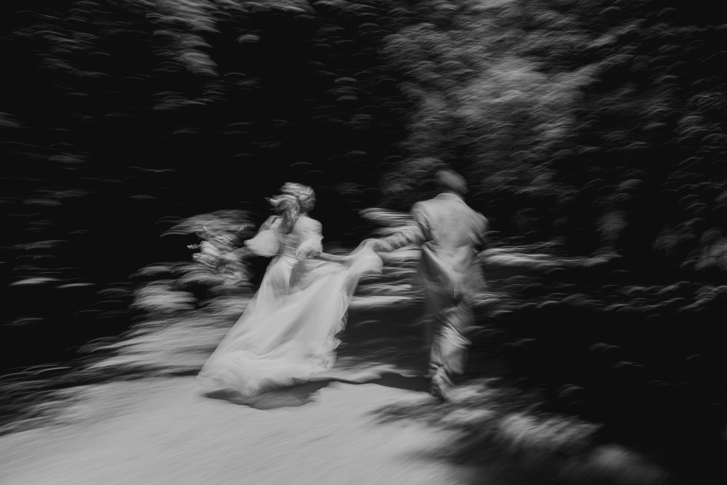 Blurred black and white photo of a bride and groom running together outdoors, capturing motion and romance.