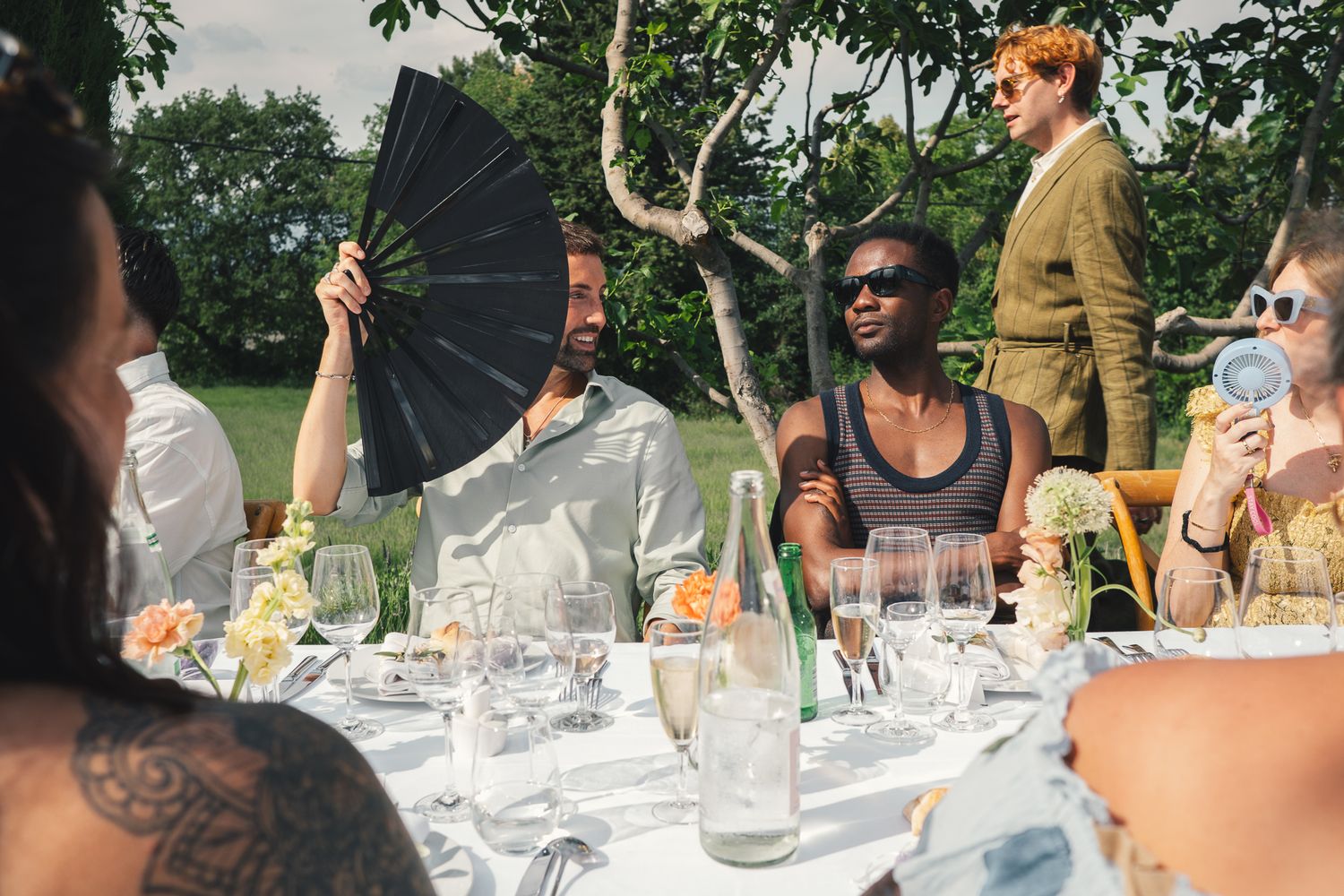 Friends laughing and socializing at an elegant outdoor garden dinner party on a sunny day.
