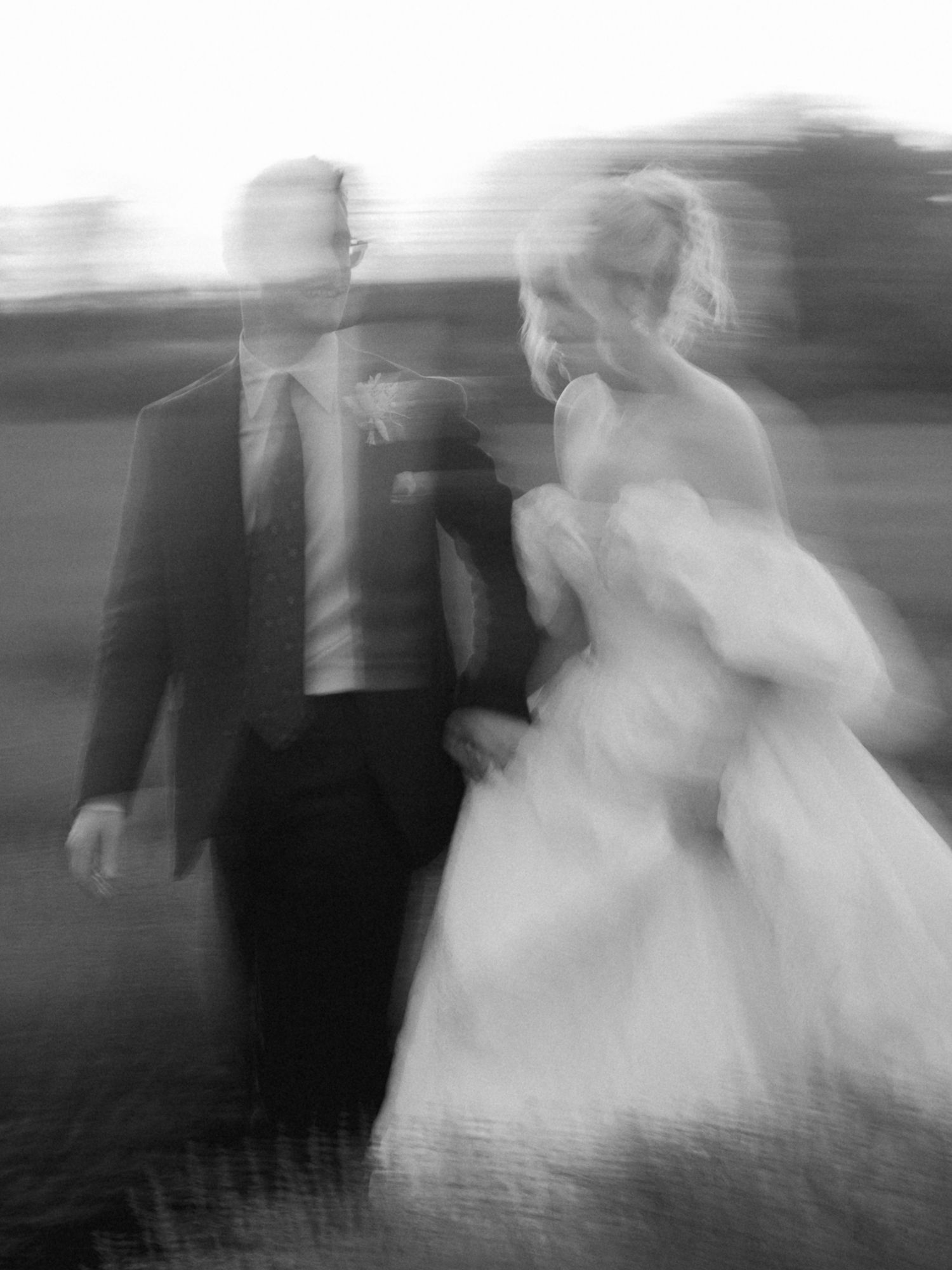 Blurred black and white photo of a bride and groom walking together on their wedding day.