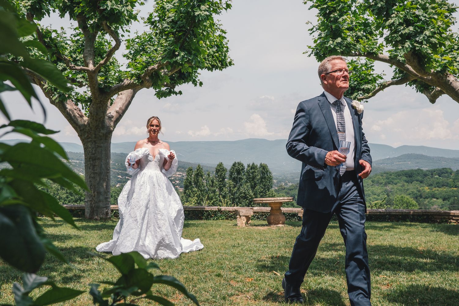 Bride in white gown and groom in blue suit share a romantic outdoor wedding moment with scenic mountain views.