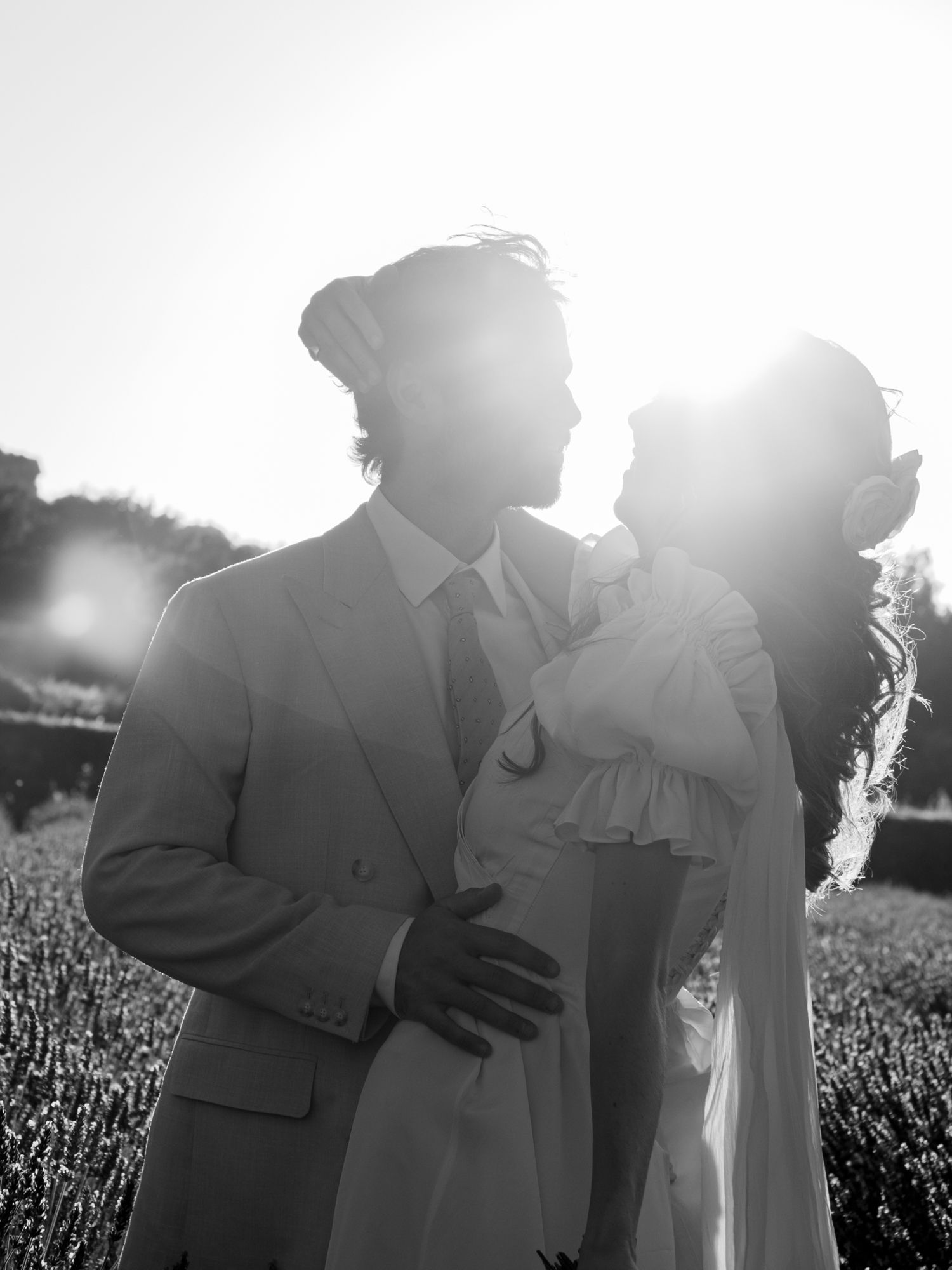 Black and white romantic portrait of bride and groom embracing in a sunlit lavender field.