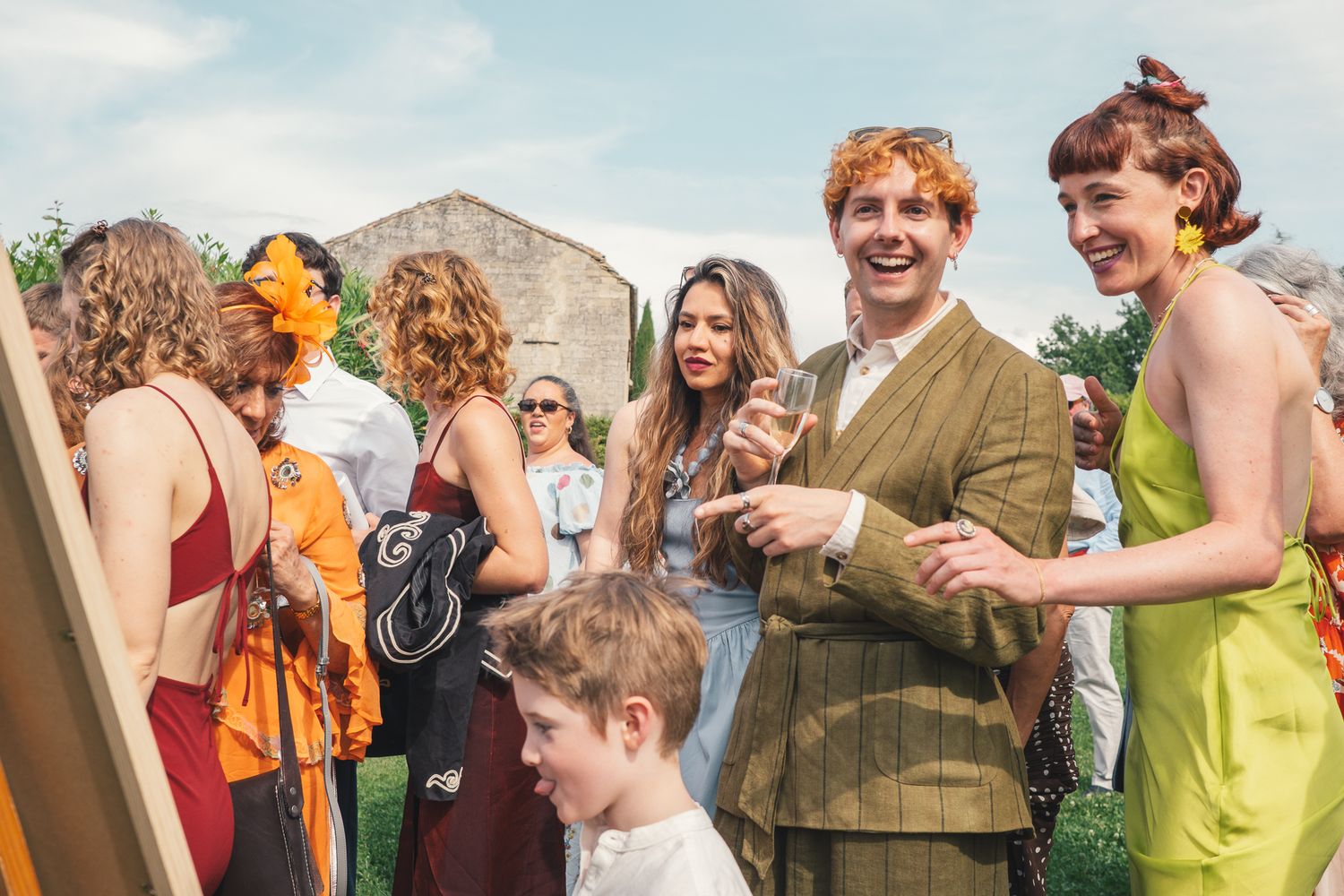 Guests in colorful outfits laugh and chat outdoors at a sunny garden party or wedding reception.