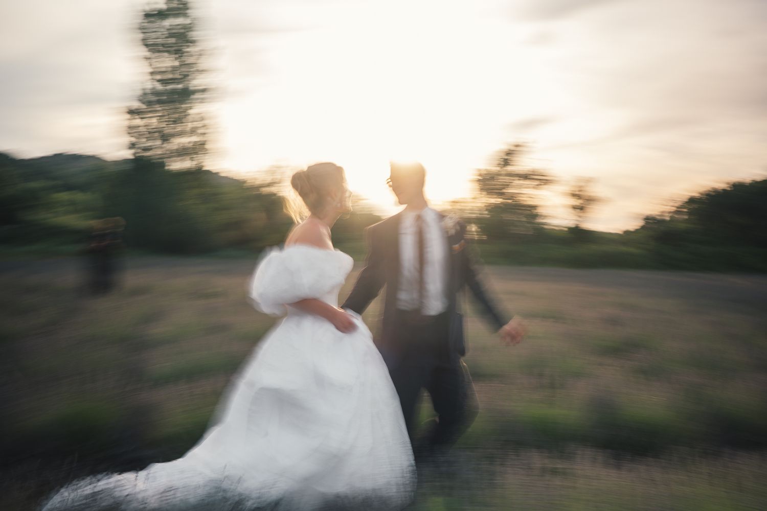 Blurred motion shot of bride and groom dancing at sunset in a lush green field on their wedding day.