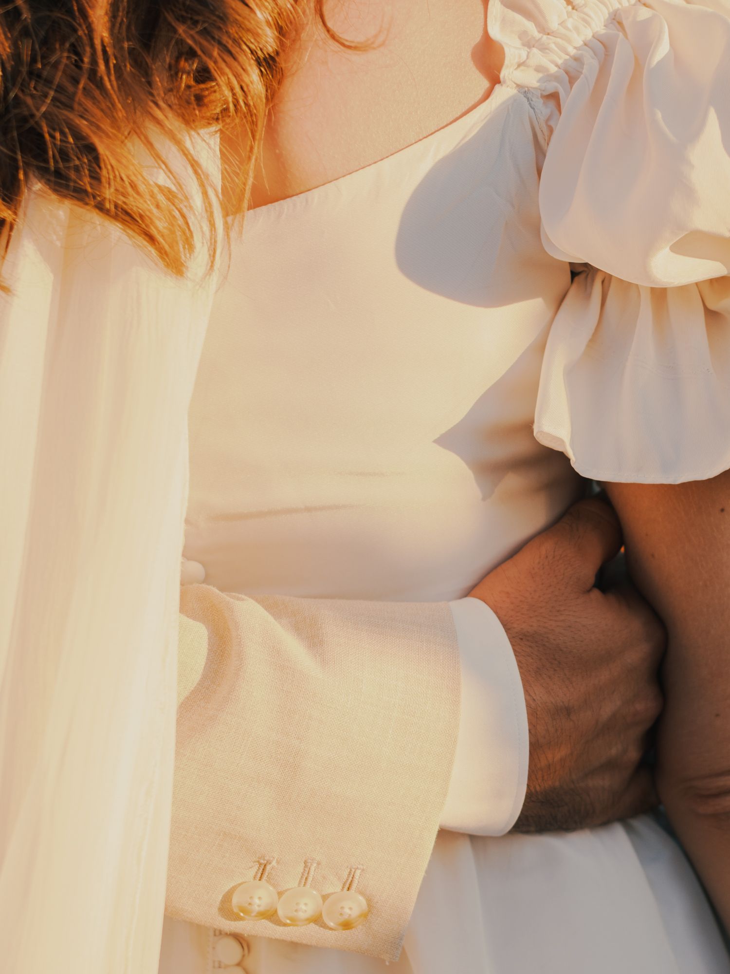 Close-up of a couple embracing in wedding attire, bride in white dress with puff sleeves, groom in white suit.
