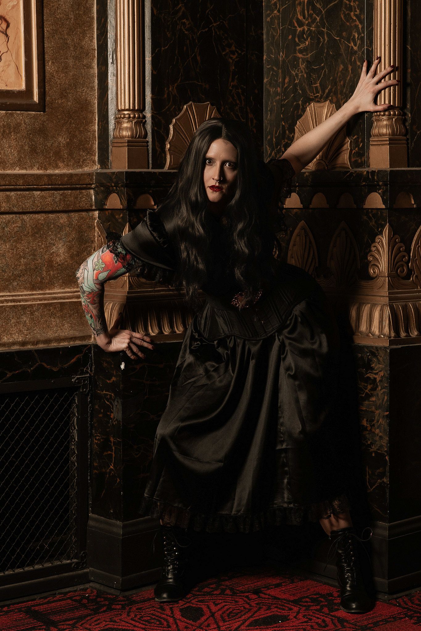 Woman in black dress and boots, posing in an ornate vintage interior.