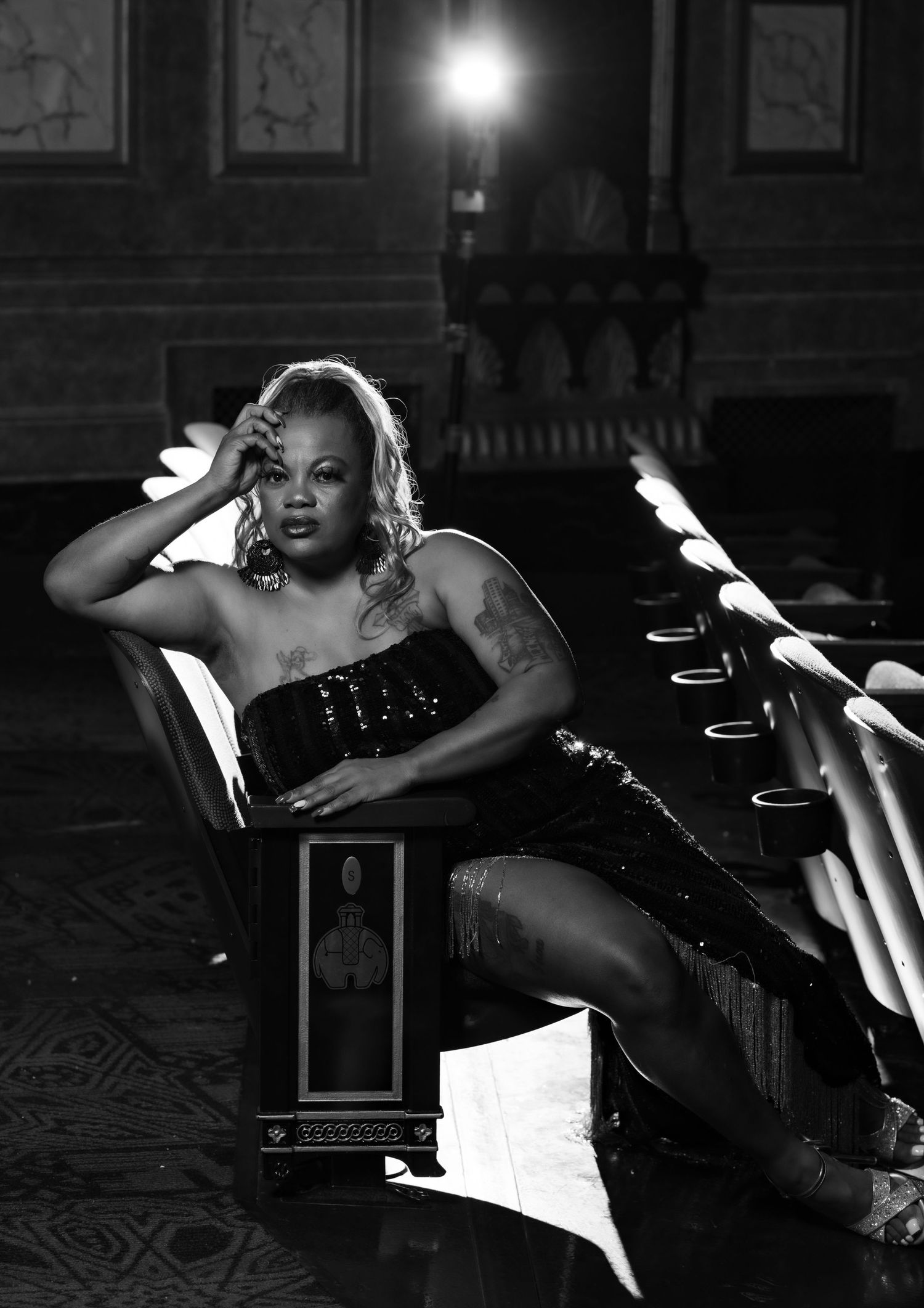 Black and white photo of a glamorous woman in sequined outfit reclining in ornate theater setting.