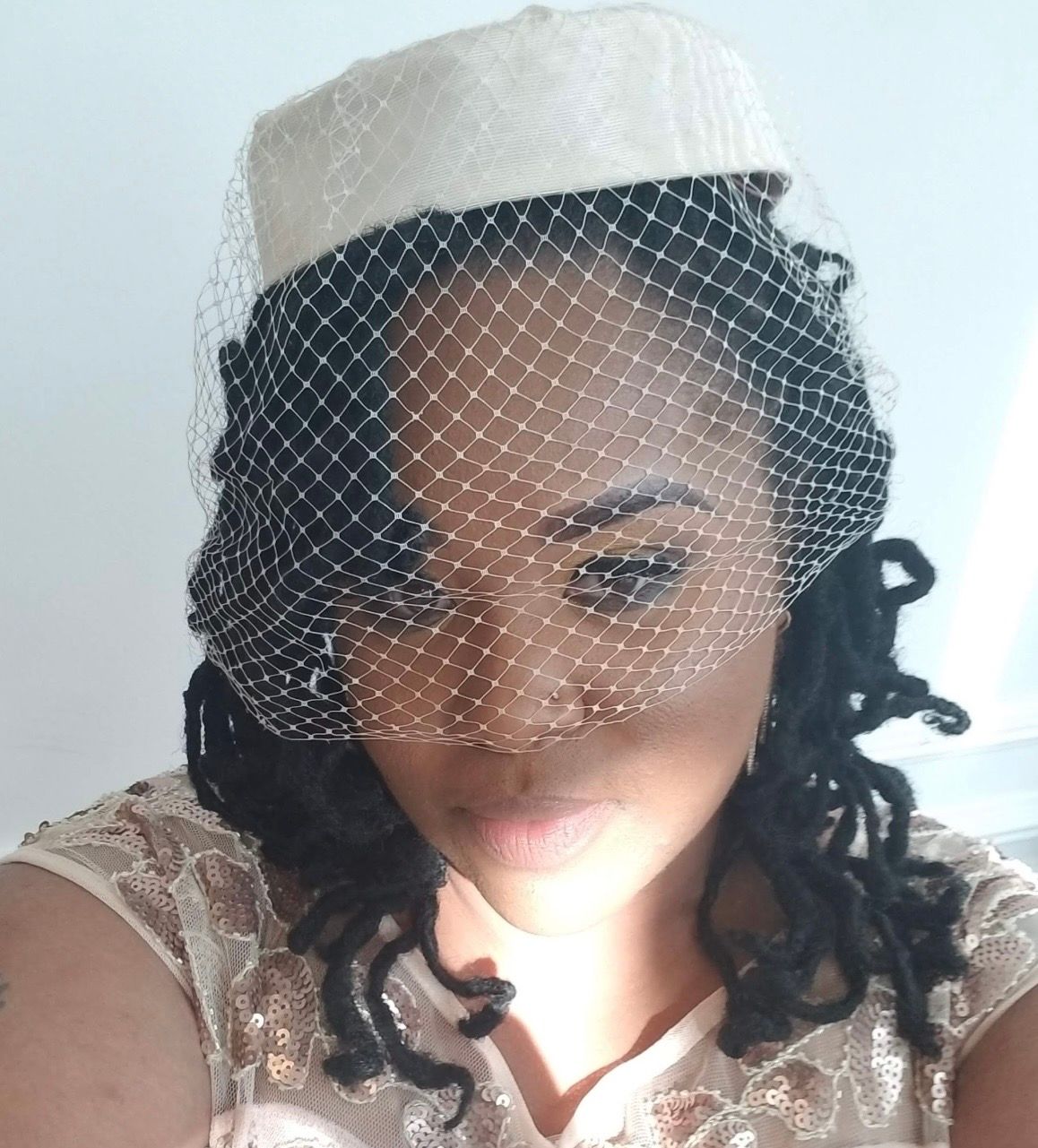 Woman wearing elegant white pillbox hat with birdcage veil for a bridal or formal occasion.