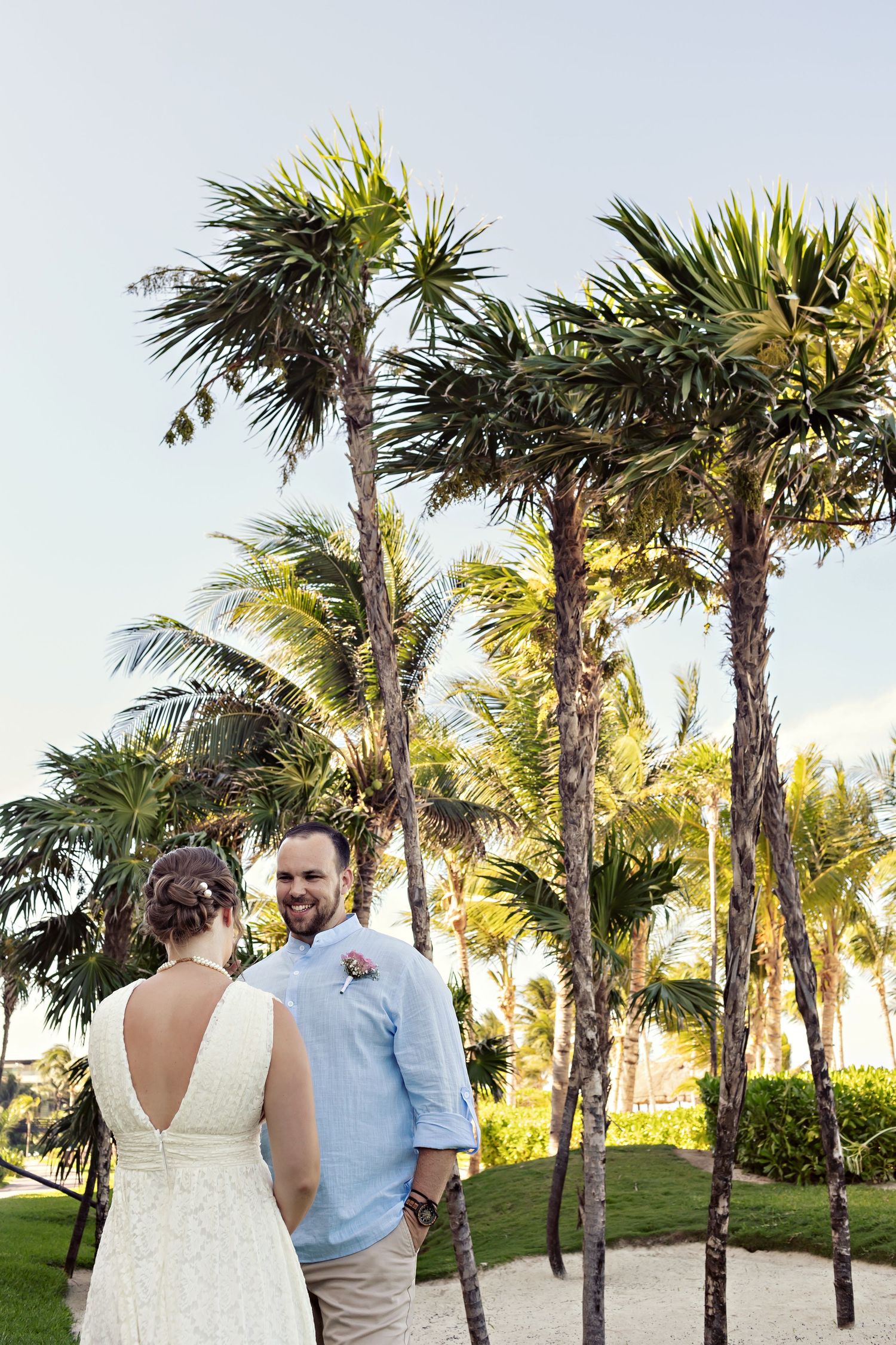 A couple walks hand in hand through a scenic path lined with tropical palm trees on a sunny day.