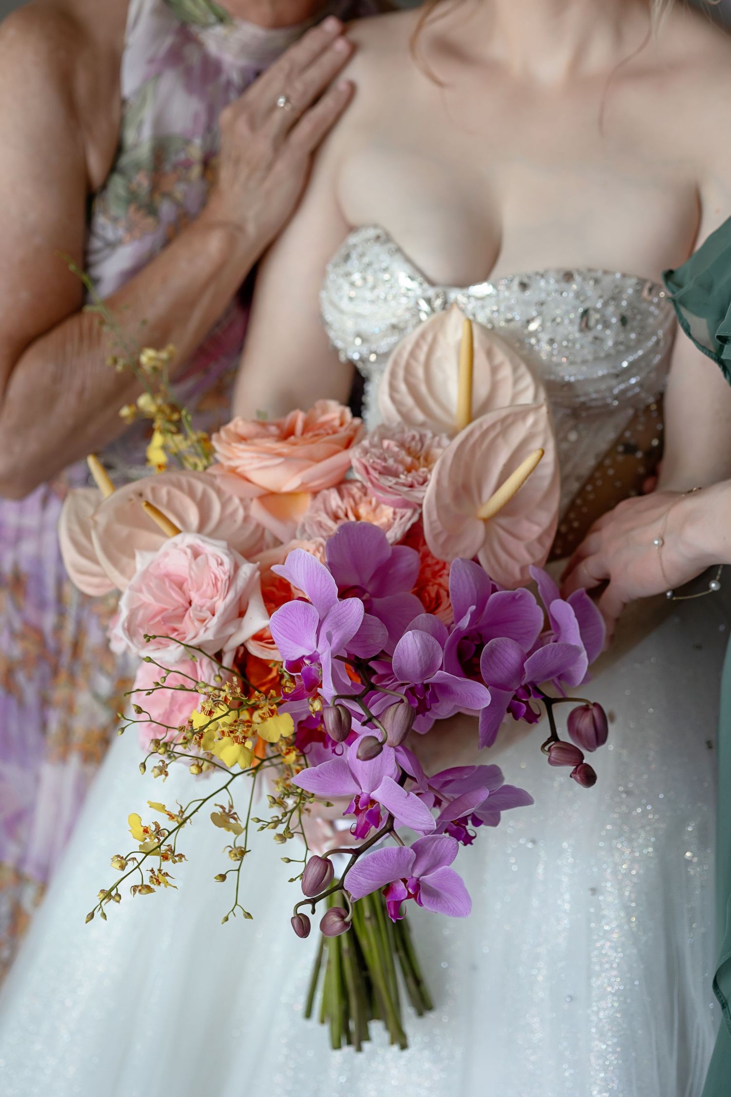 Bride holding a vibrant wedding bouquet with purple orchids, peach anthuriums, and roses in a beaded strapless gown.