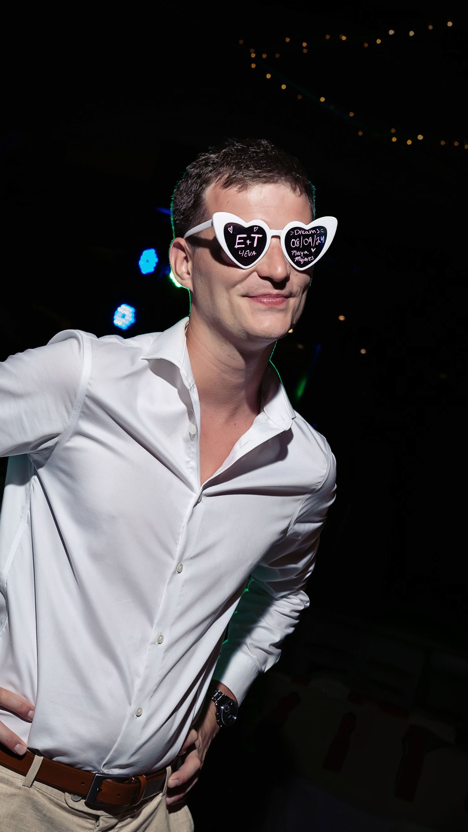 Person in white button-down shirt wearing heart-shaped sunglasses poses at a nighttime event.