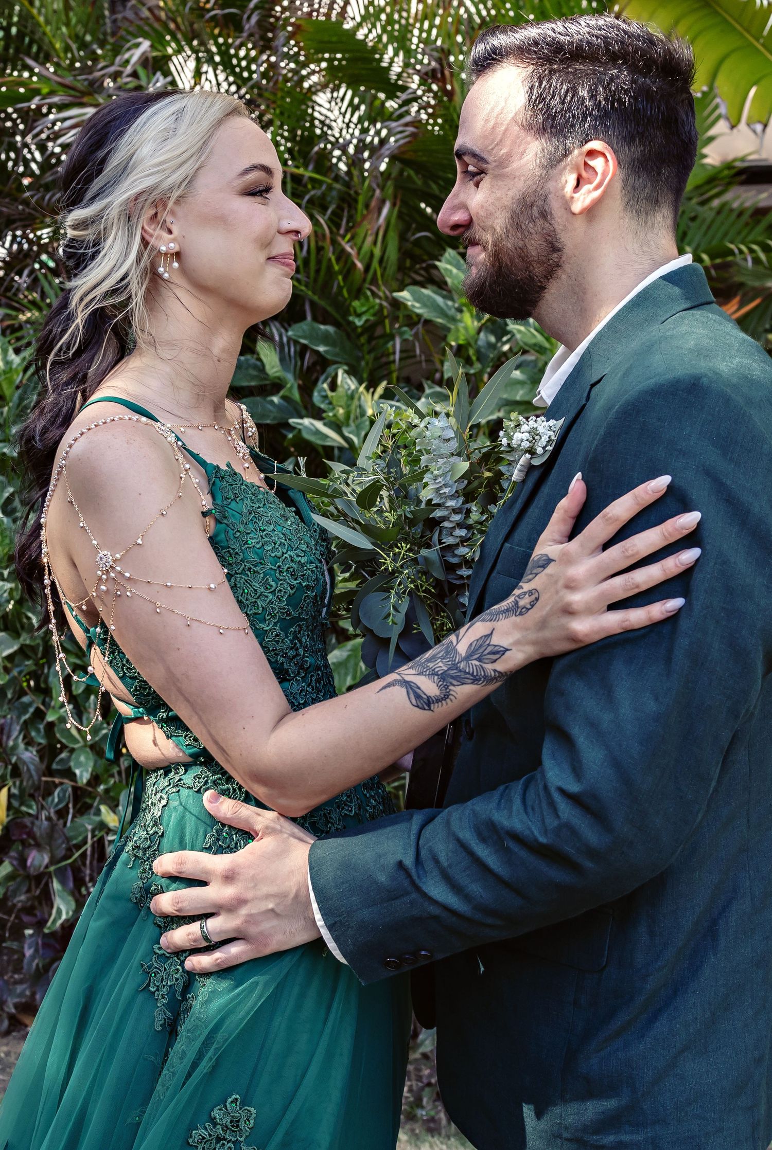 A couple in formal attire sharing an intimate moment against a lush tropical garden backdrop.