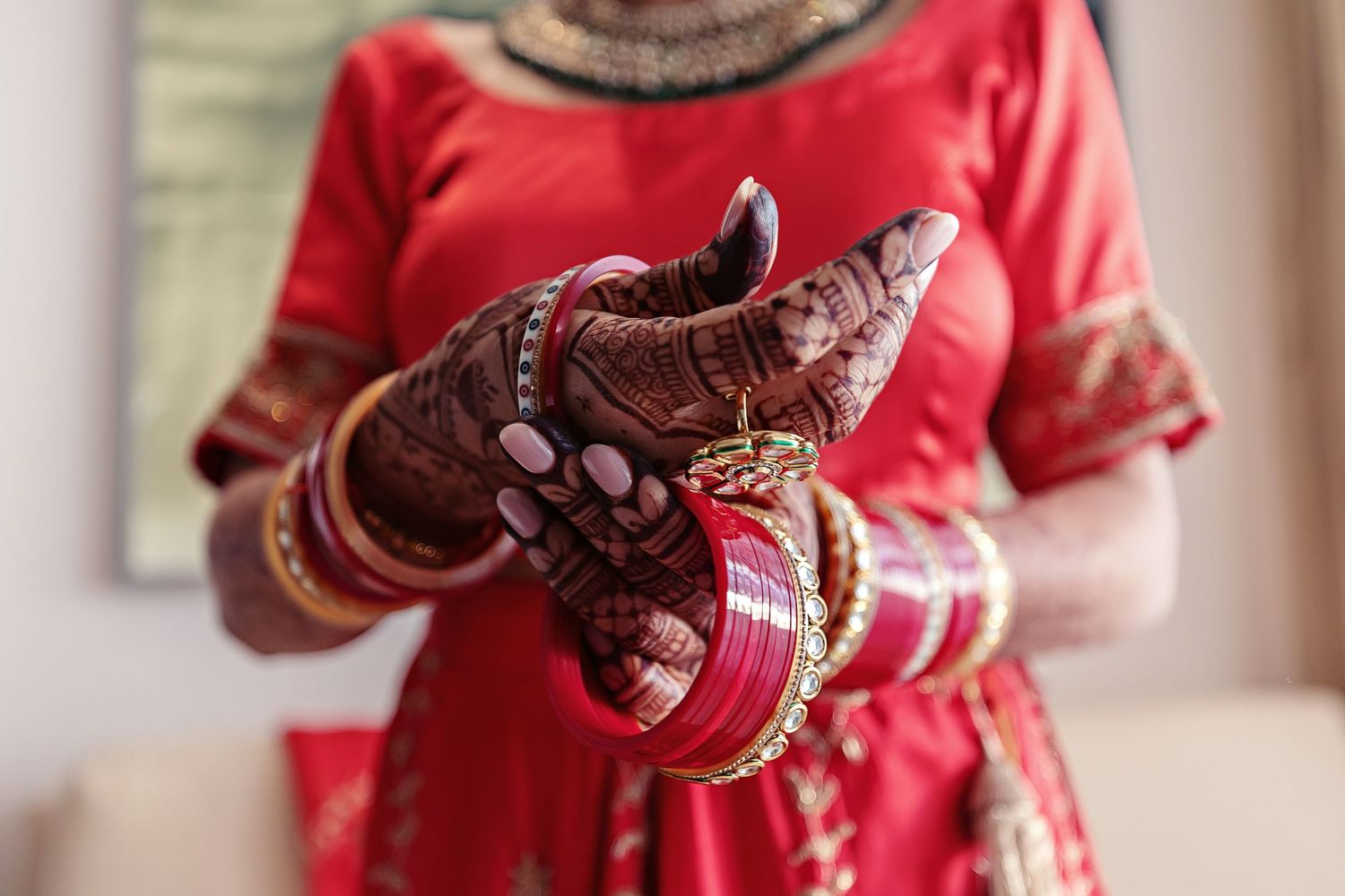 Indian bride in red dress adjusting gold bangles and bracelets on hands adorned with intricate henna mehndi design.