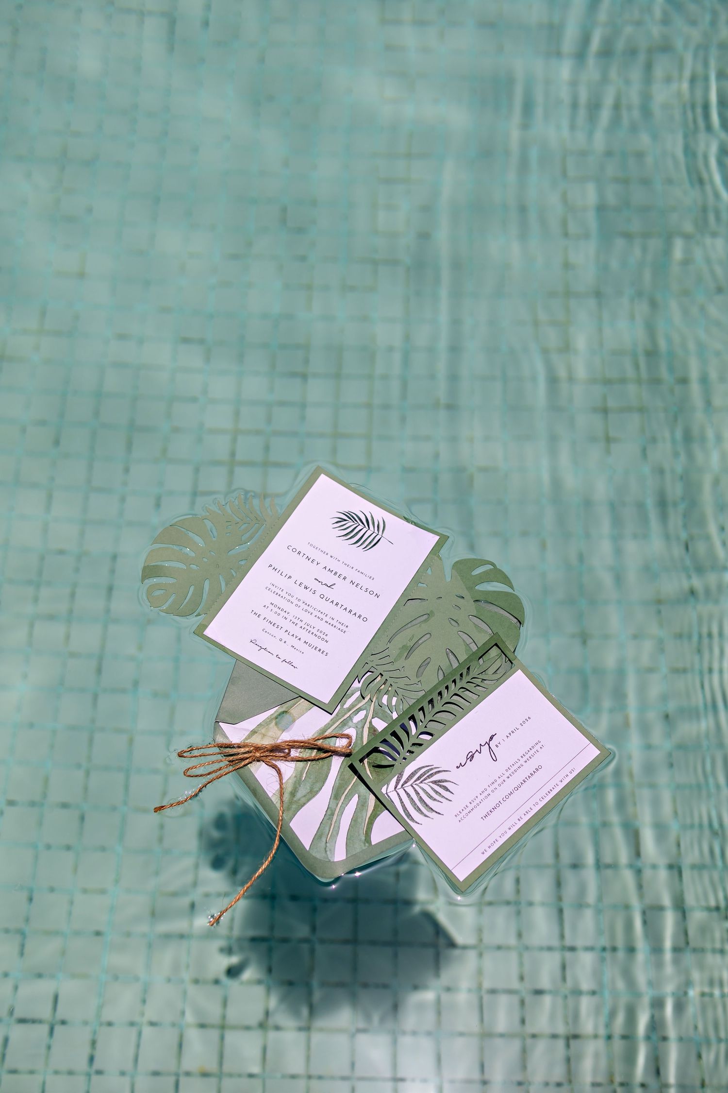 Tropical wedding invitation suite with monstera leaf accents floating in a turquoise pool.