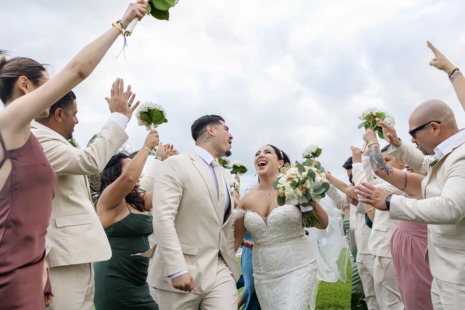Wedding party celebrating with raised champagne glasses and bouquets during outdoor celebration.