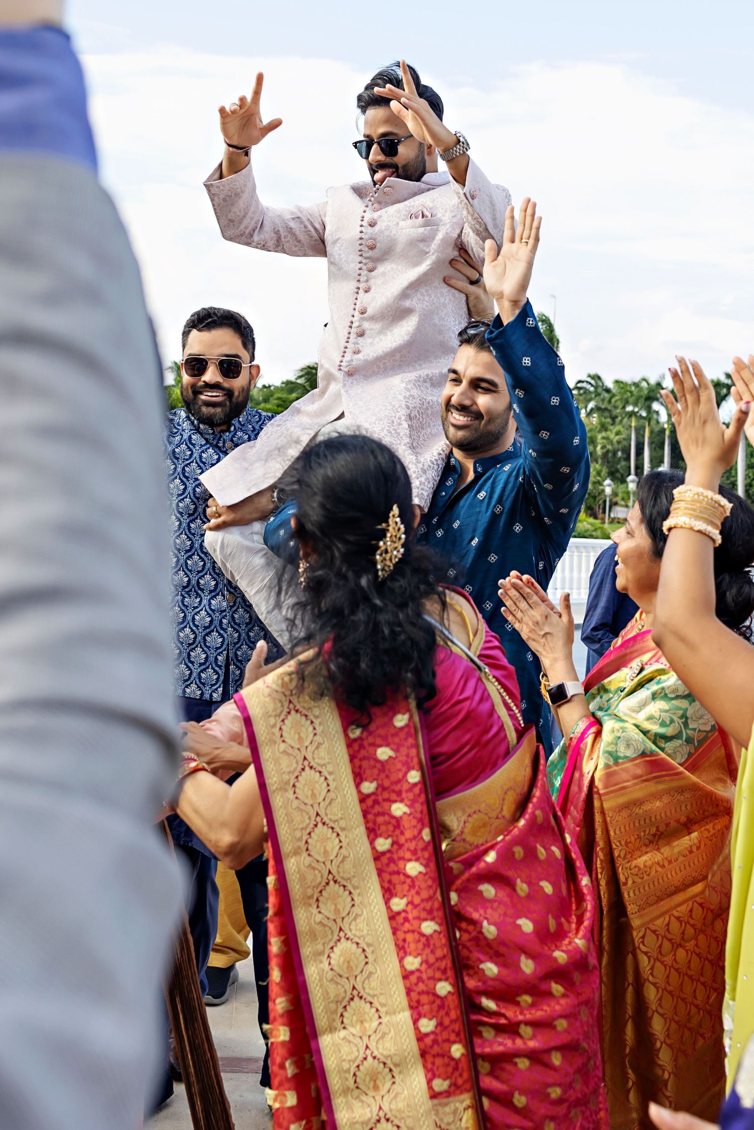 Guests dance and celebrate joyfully at an outdoor Indian wedding celebration wearing traditional colorful attire.