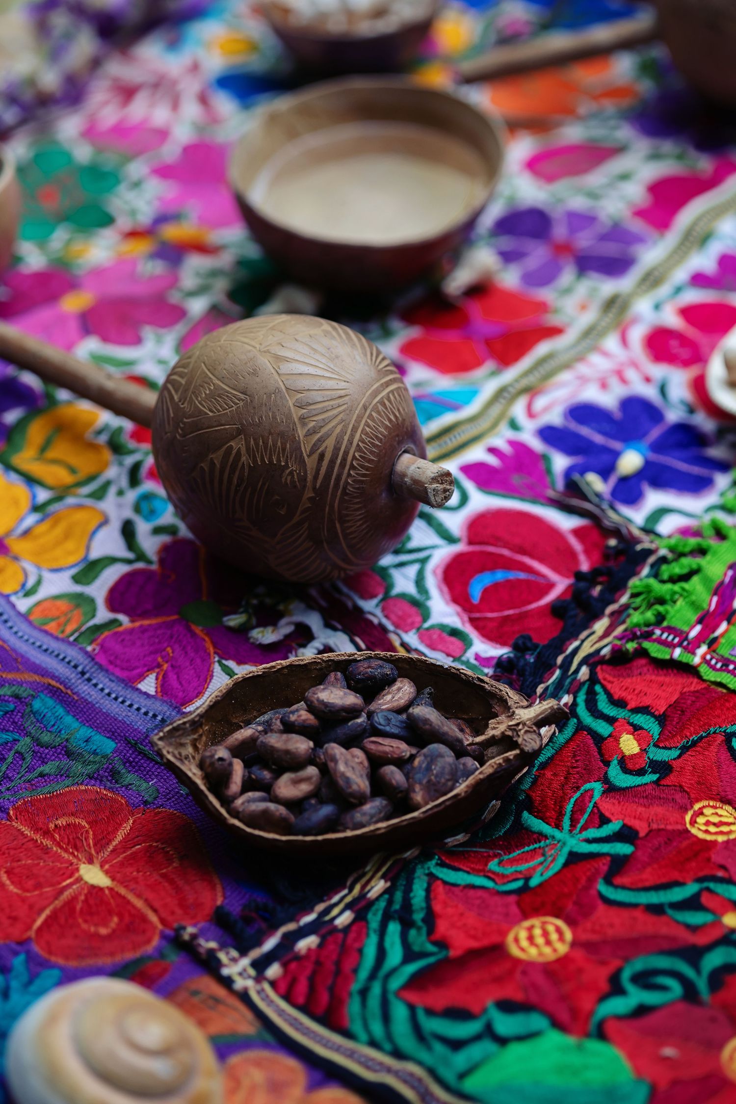 Traditional Mexican cacao ball and chocolate beans displayed on vibrant embroidered textile with ceremonial elements.
