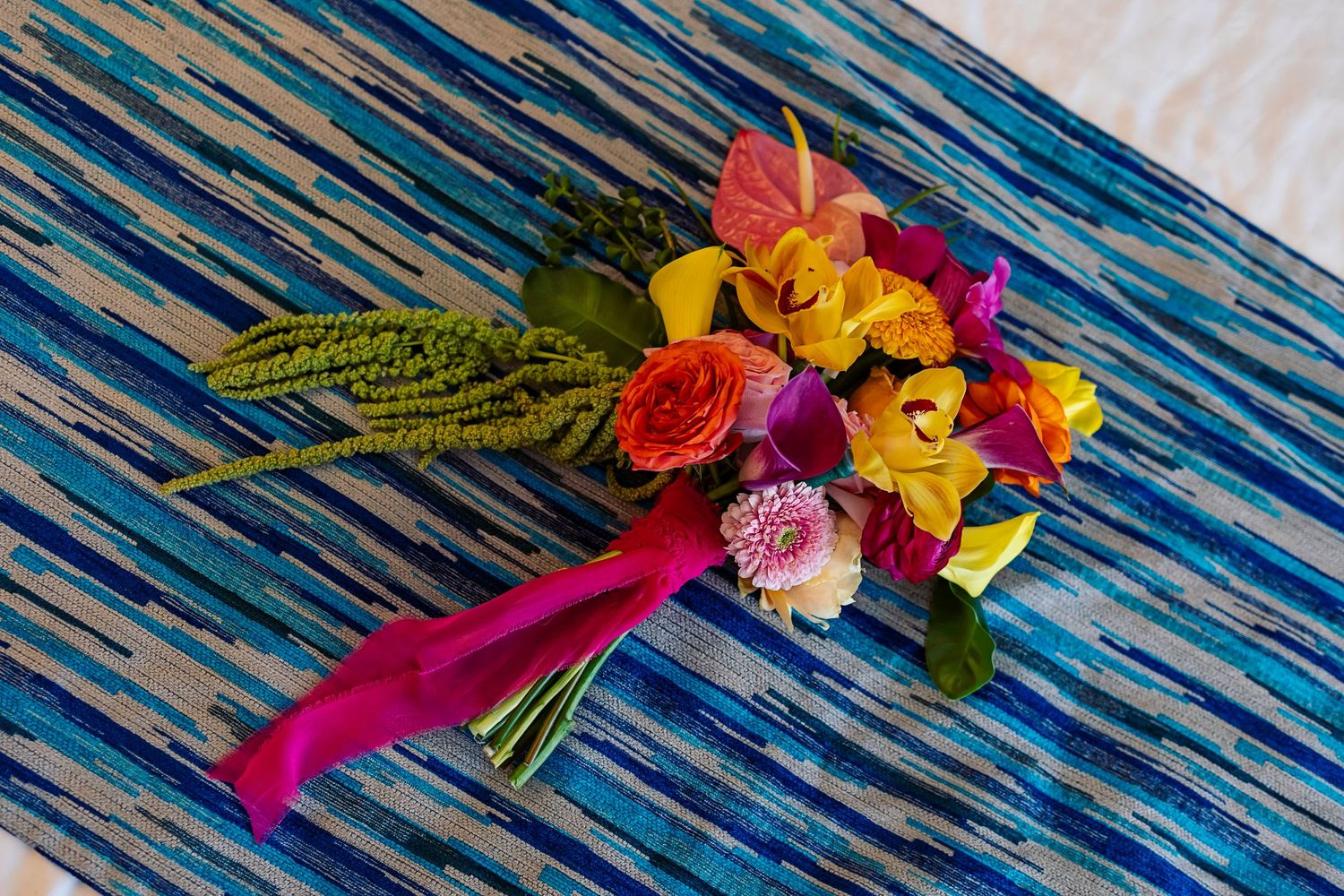 Vibrant tropical wedding bouquet with colorful flowers on a blue striped fabric runner.