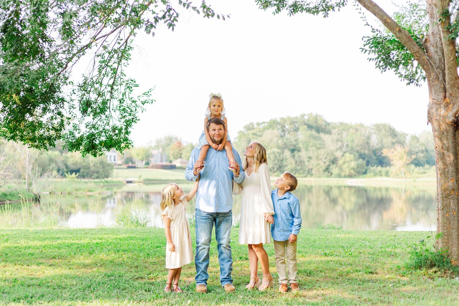 Family of five posing together near a lake with trees in the background for family photo session near Patrick Square in Clemson, SC
