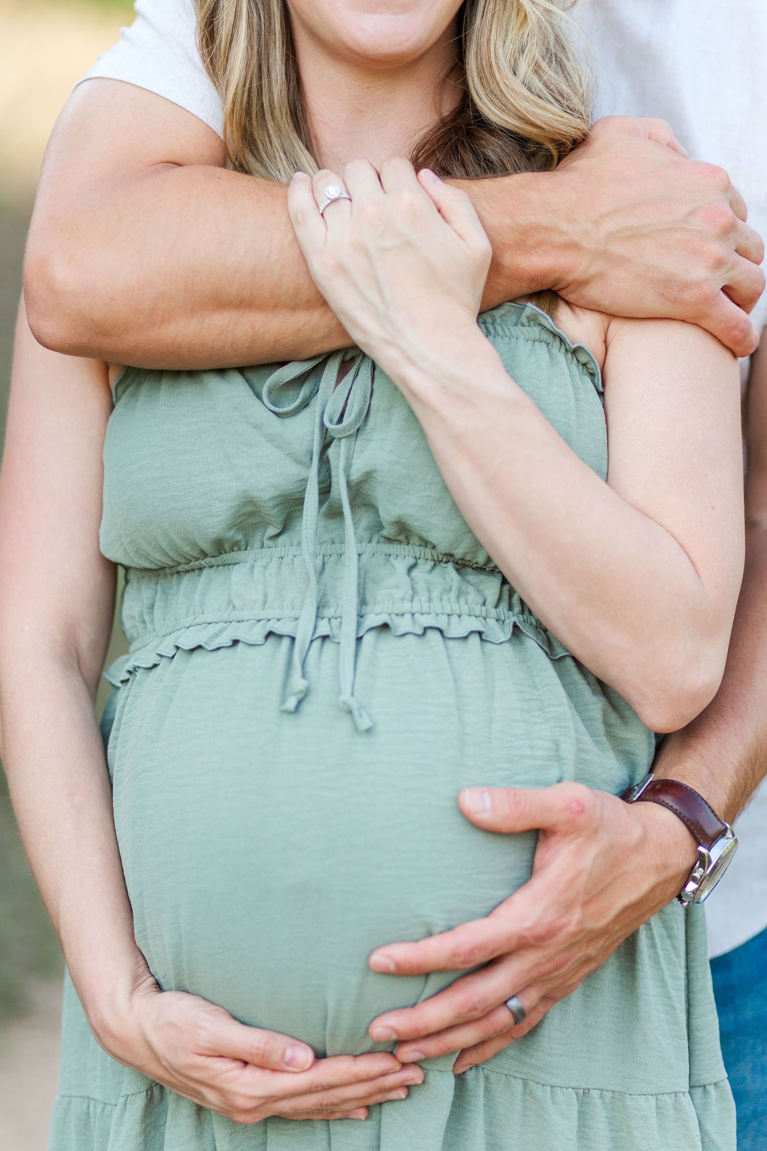 Close-up shot of hands gently cradling a pregnant belly in a sage green maternity dress for maternity session in Clemson, SC
