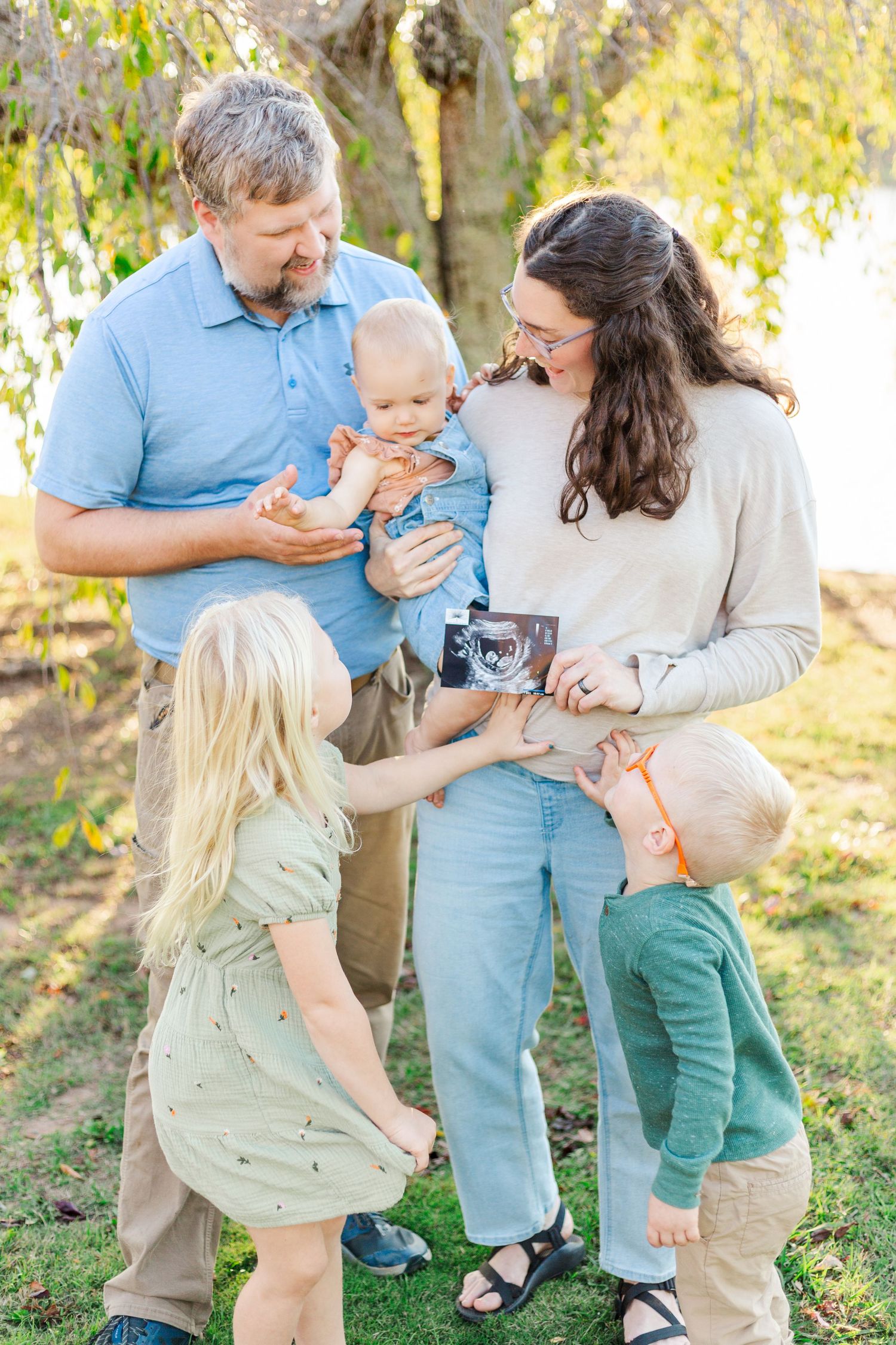 Family enjoying tender moments together outdoors in a sunlit garden setting with natural lighting and greenery.