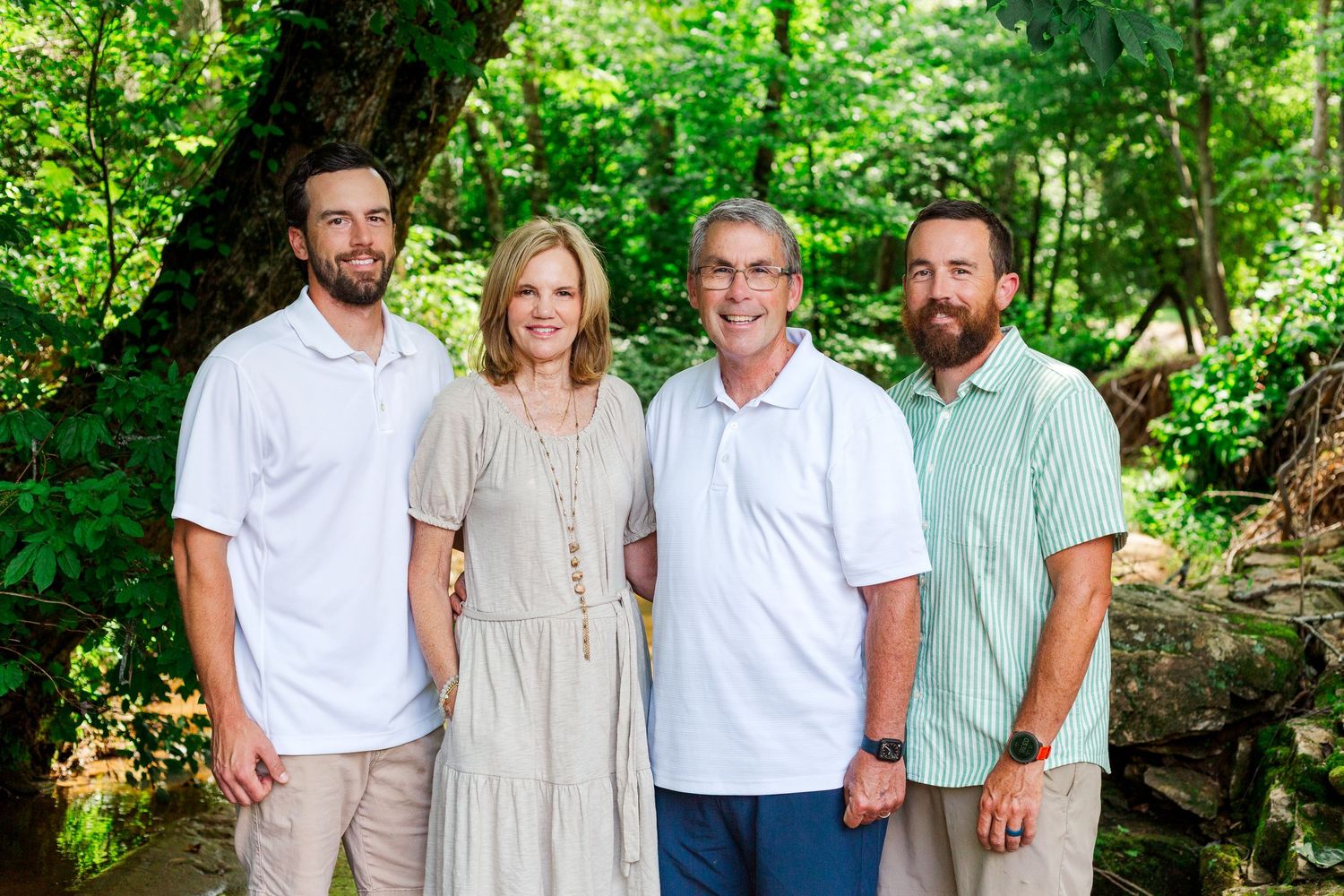 Four people in casual summer attire pose together outdoors against a lush green garden background.