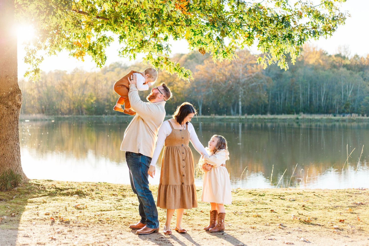 Family enjoying a peaceful autumn moment by a serene lake under golden sunlight filtering through tree branches.