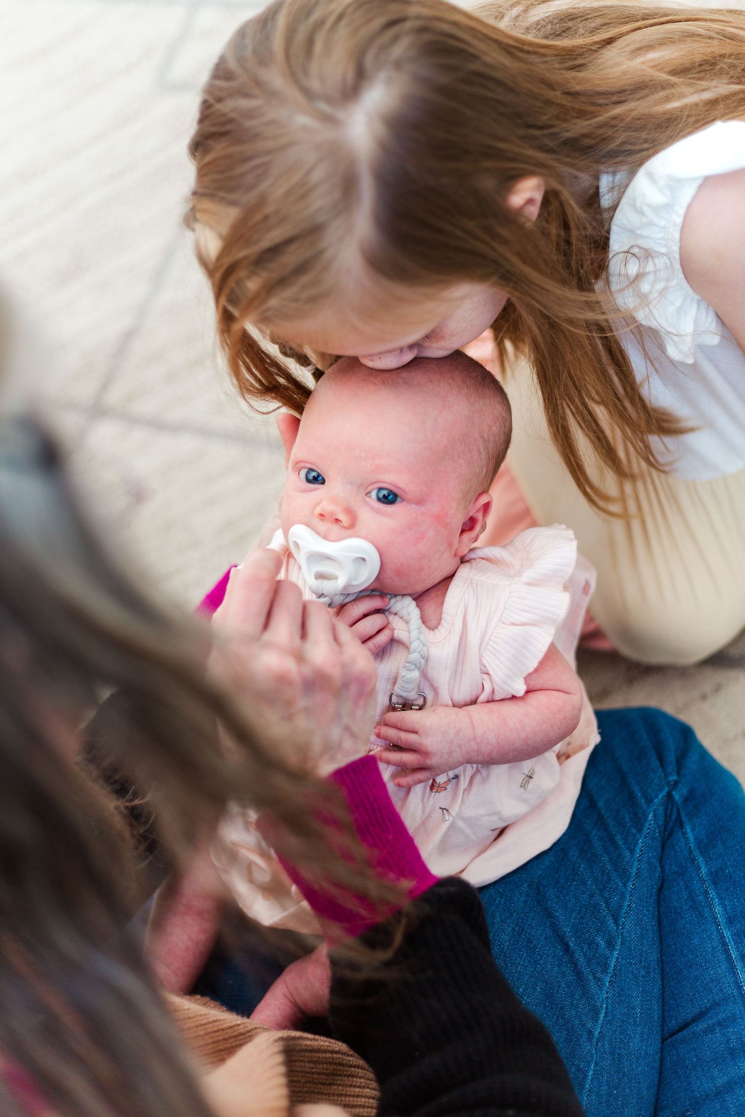 A tender moment as a baby with a pacifier wearing a white outfit is held closely in someone's arms.