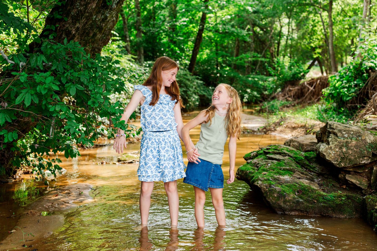 Families enjoy a summer day together wading in a shallow forest creek.