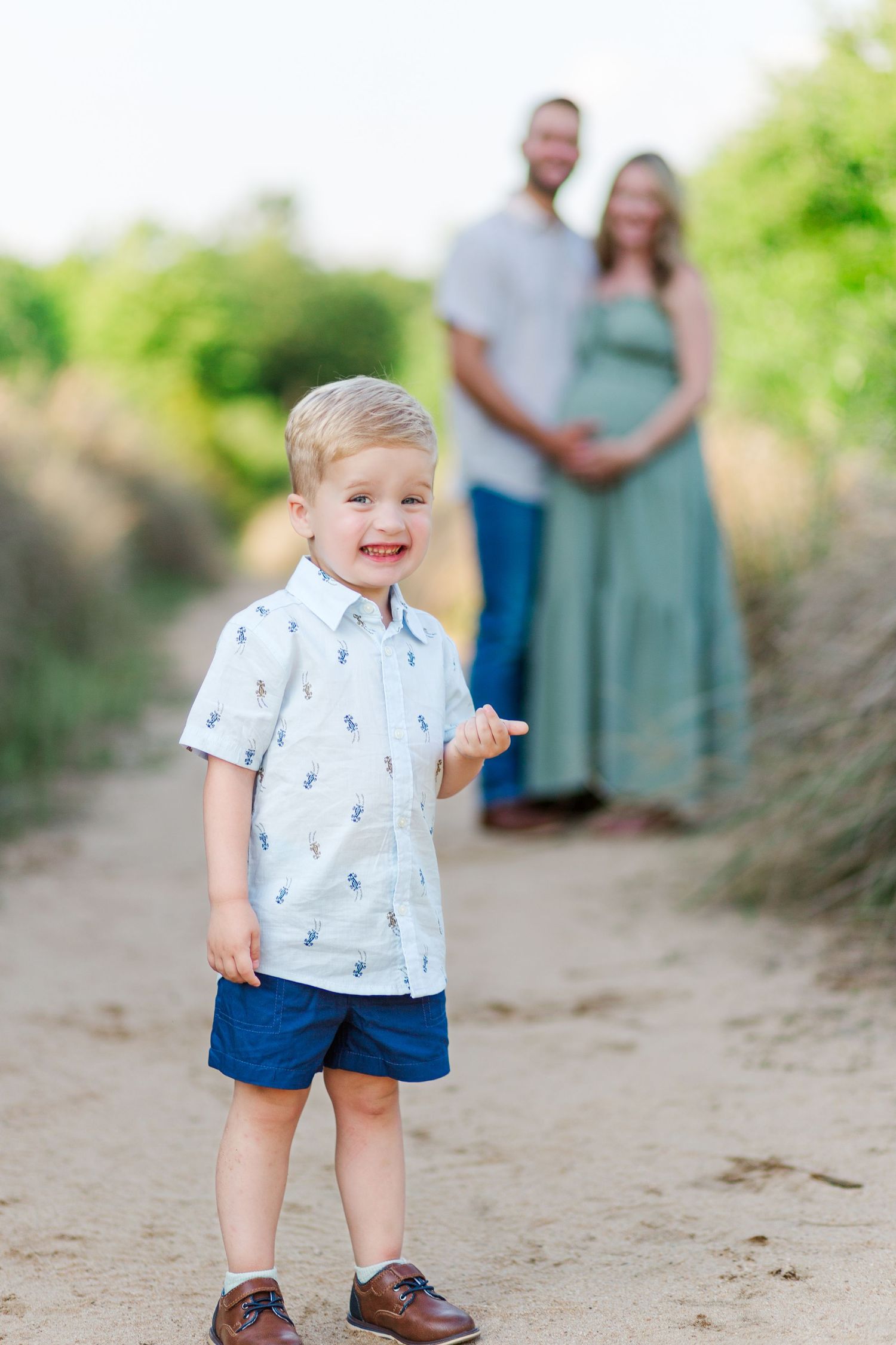 A young child in a patterned shirt and blue shorts smiles in Clemson, SC for a spring family photo session