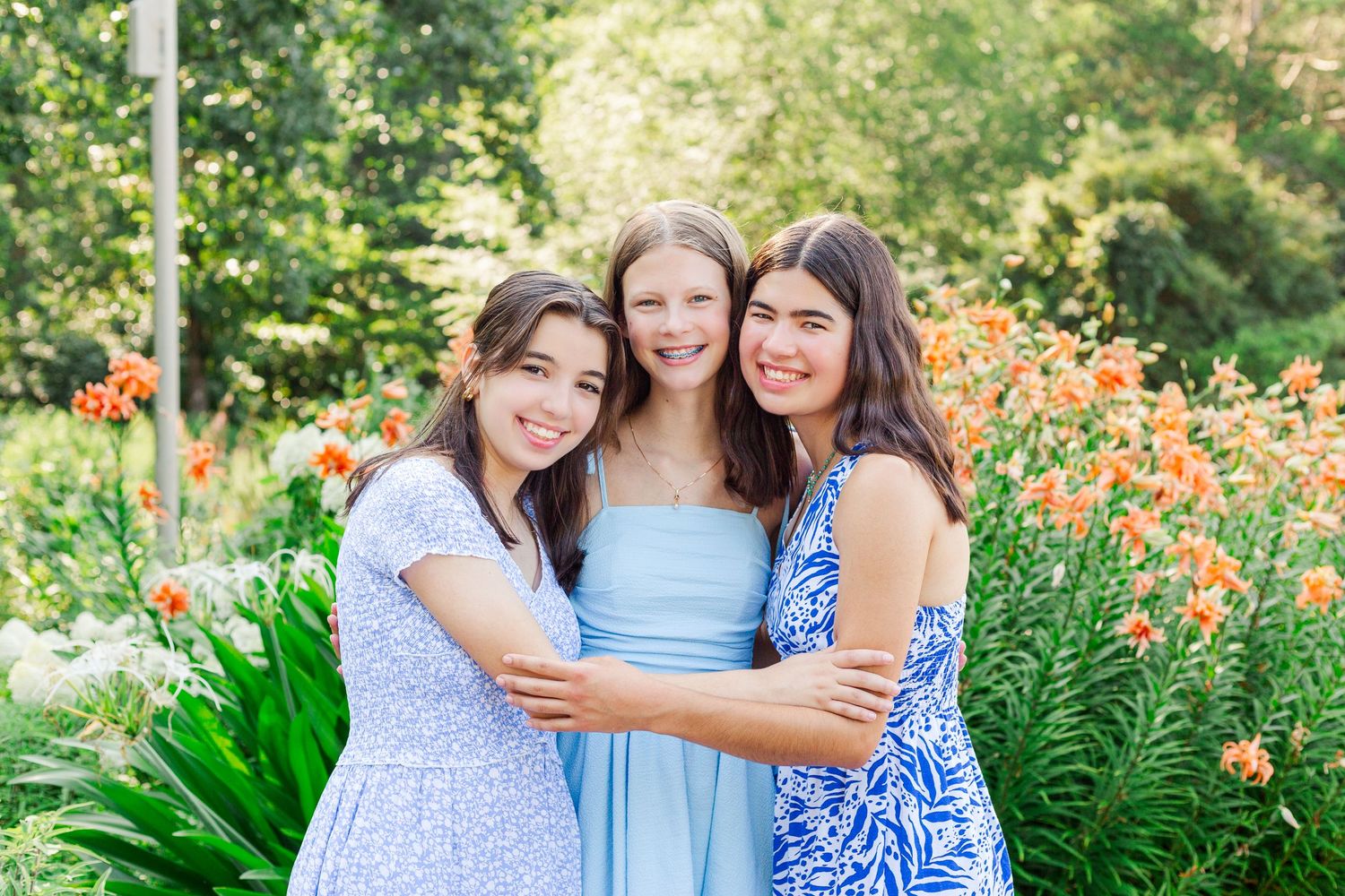 Three high school seniors in summer dresses embrace while standing in the Botanical Gardens in Clemson, SC.