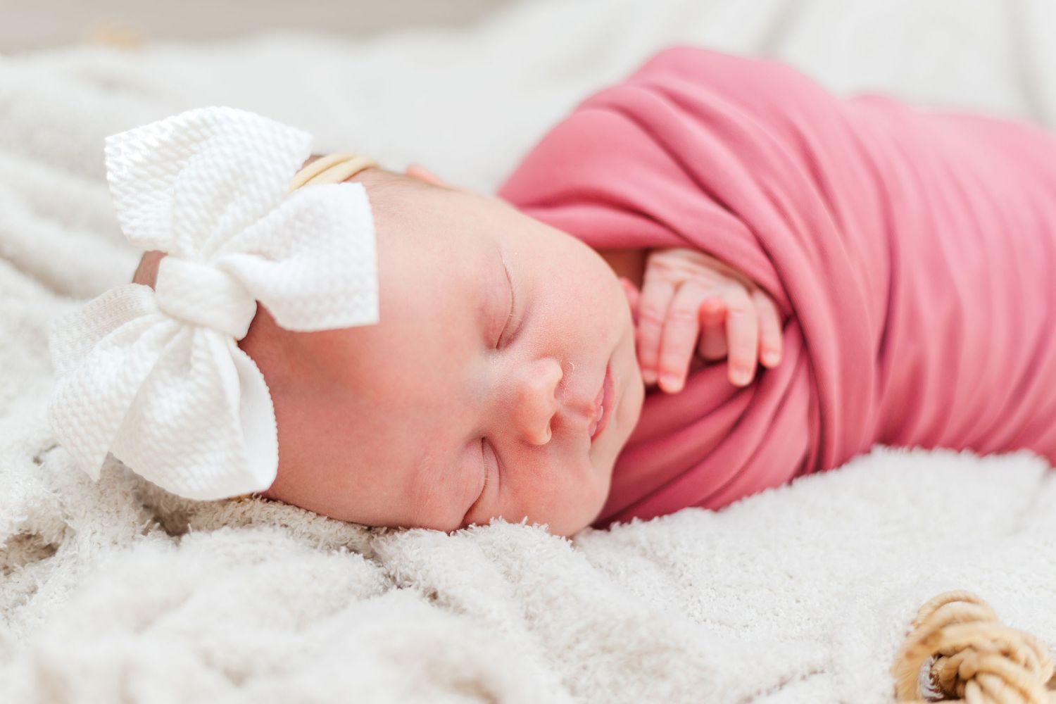 Baby sleeping peacefully on white blanket next to plush teddy bear companion.