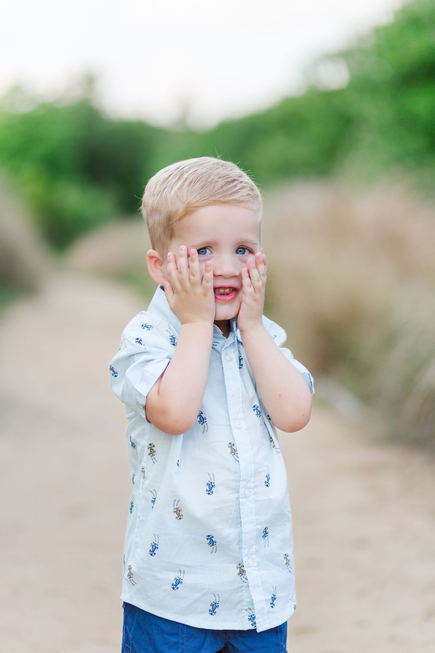 A child in a blue and white patterned shirt plays peek-a-boo for family photo session in Clemson, SC
