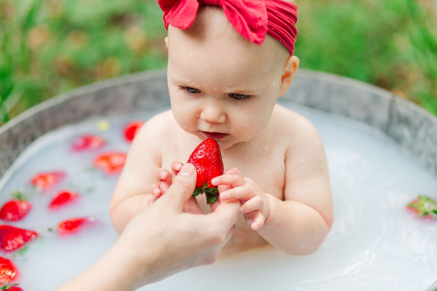 Baby in metal tub wearing red bow has strawberry milk bath photo session in Greenville, SC