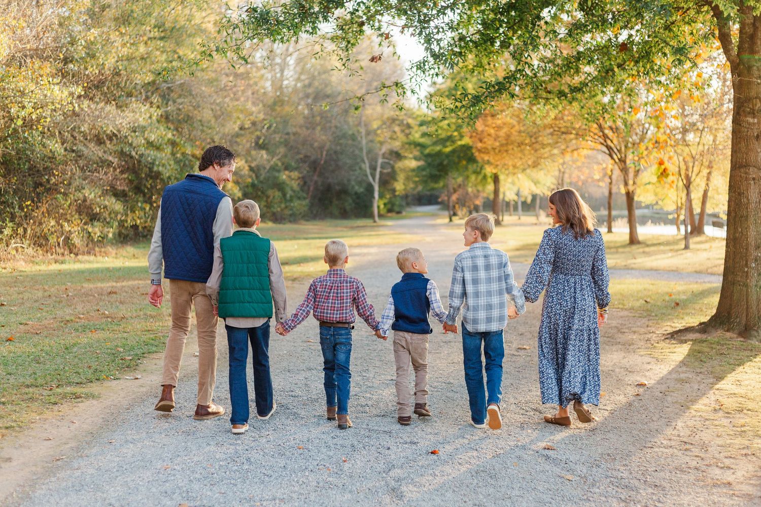 A group of people walking together on a sunlit dirt path through a park during golden hour.