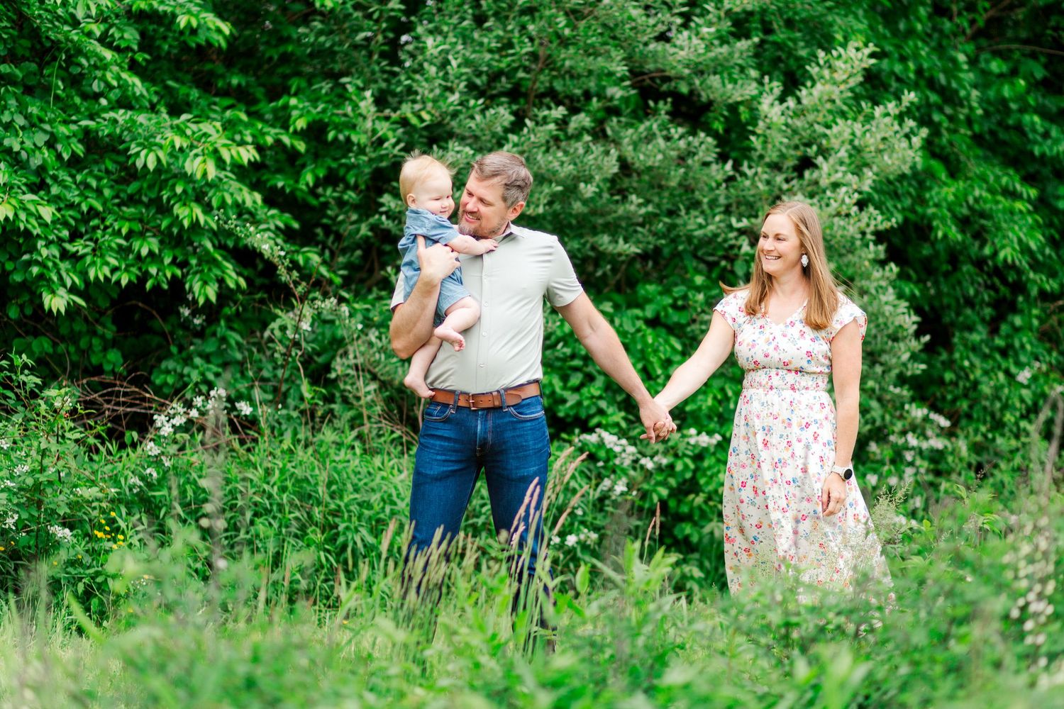 A couple in a summer meadow enjoys a walk together through tall grass and lush green foliage in Hendersonville, NC taken by a Clemson, SC