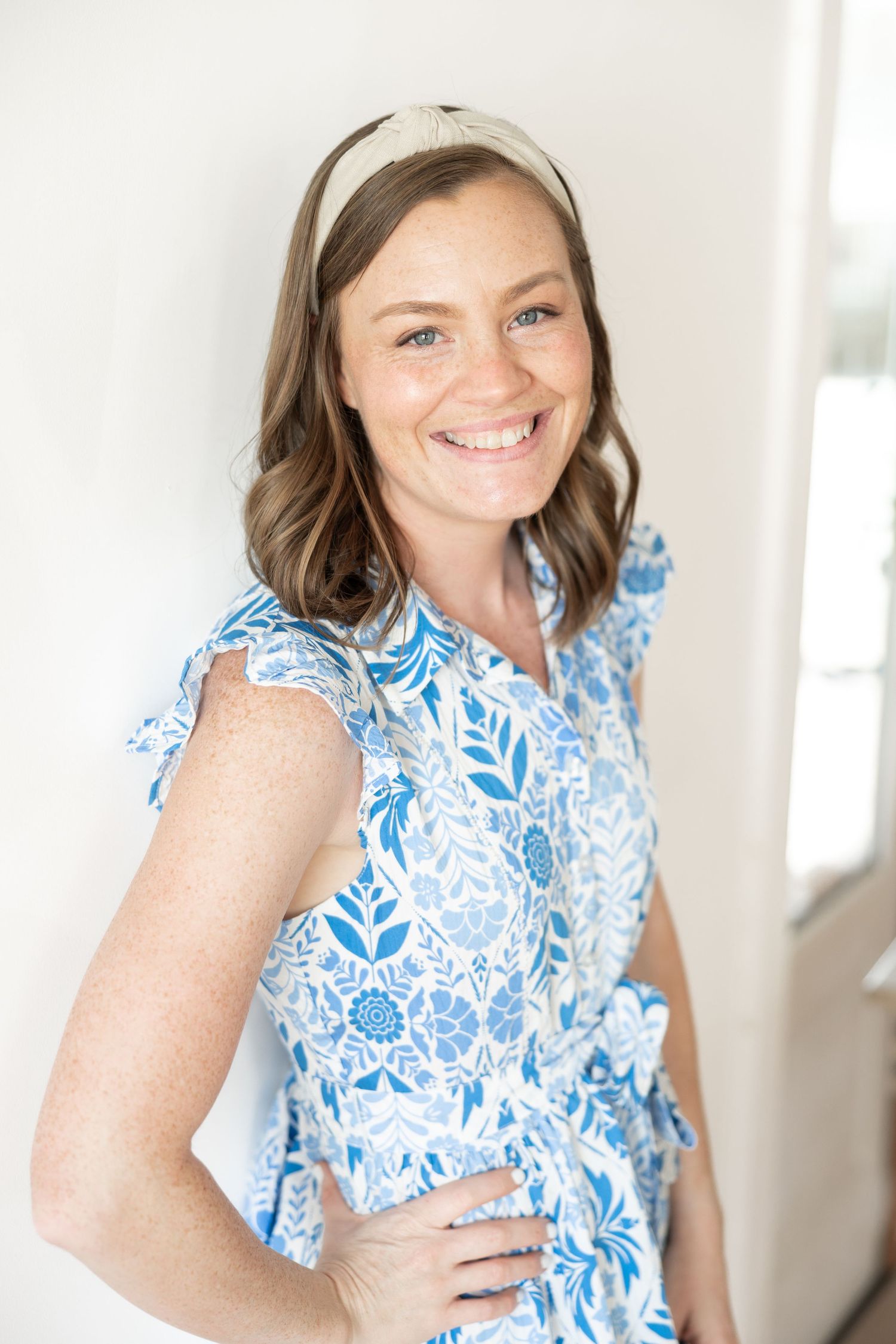 A person wearing a blue and white floral print dress poses for a series of casual portraits in a bright indoor setting.