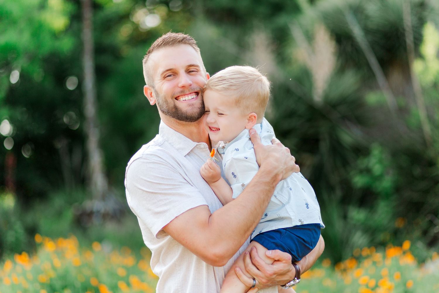 A father and young child share joyful moments together in a garden filled with yellow wildflowers.