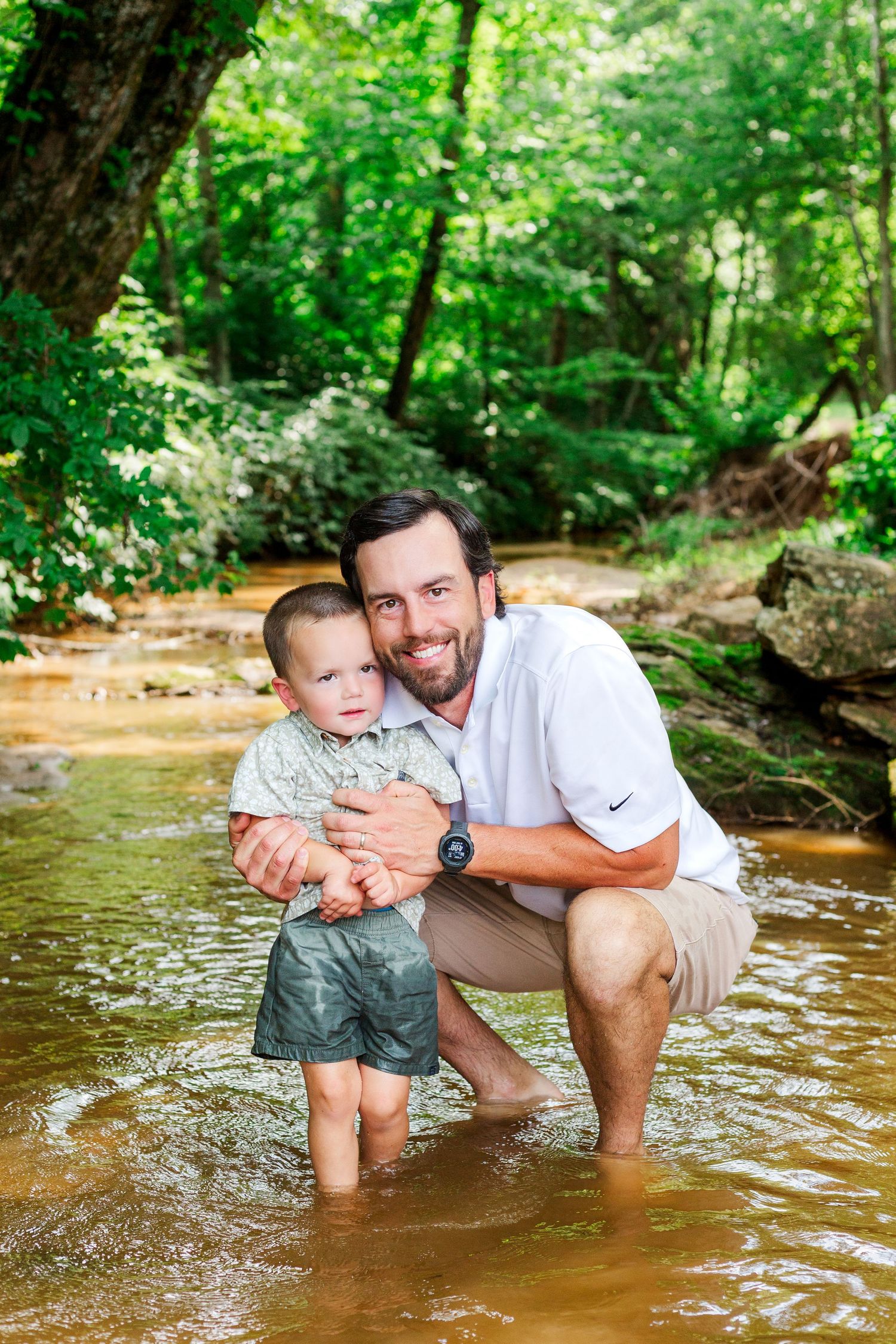 Two people share a tender moment while standing in shallow creek waters surrounded by trees.