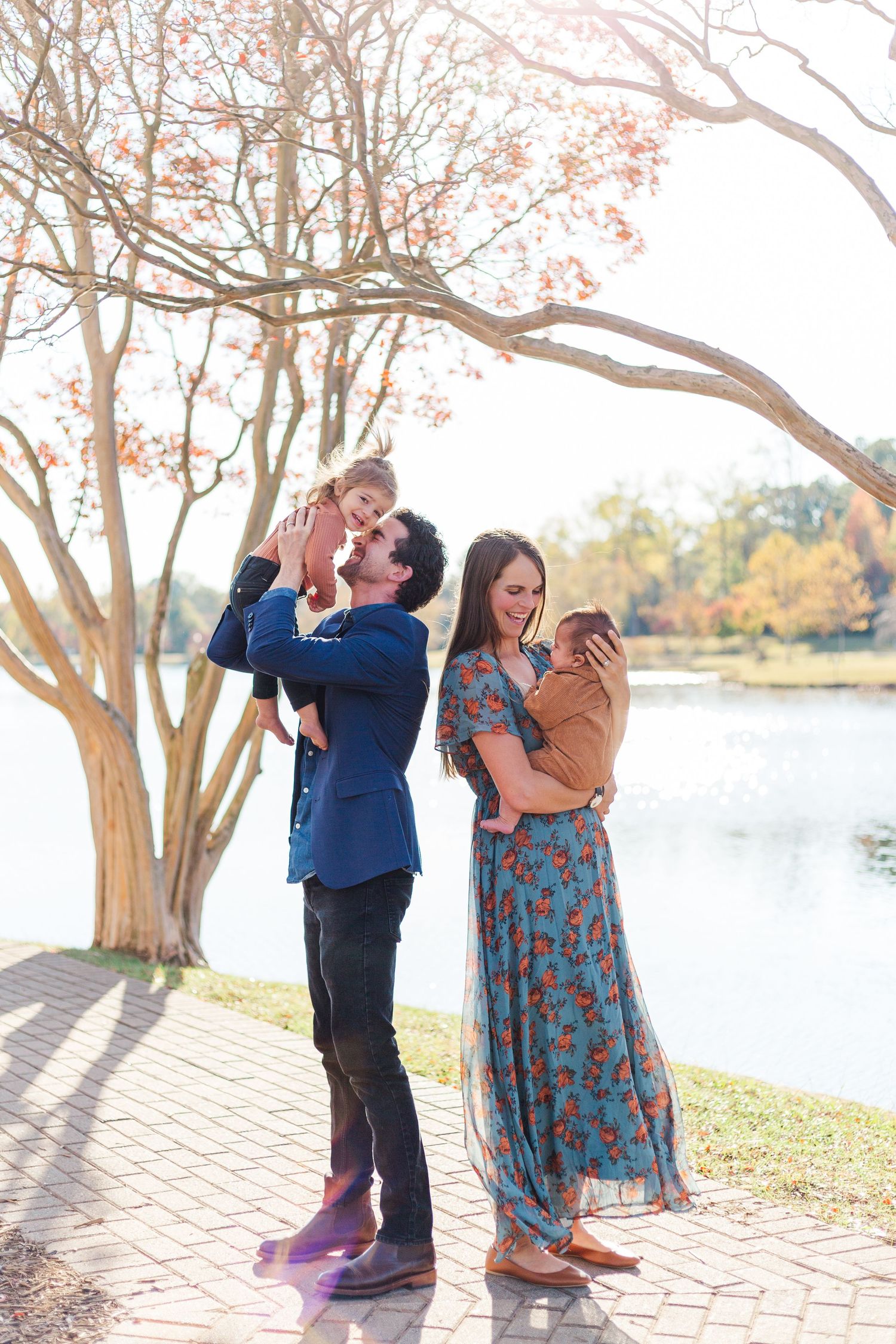 Family enjoys a sunny autumn day by a lake with flowering trees in the background.