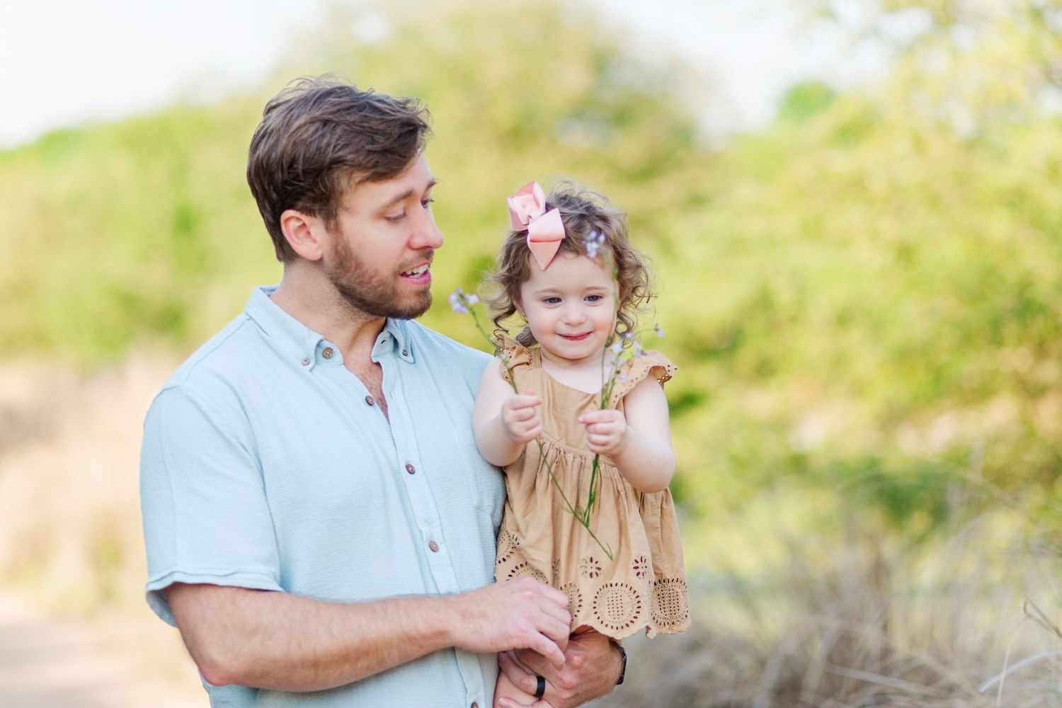 A father and daughter share joyful moments together in a sunlit outdoor setting during a family photoshoot.