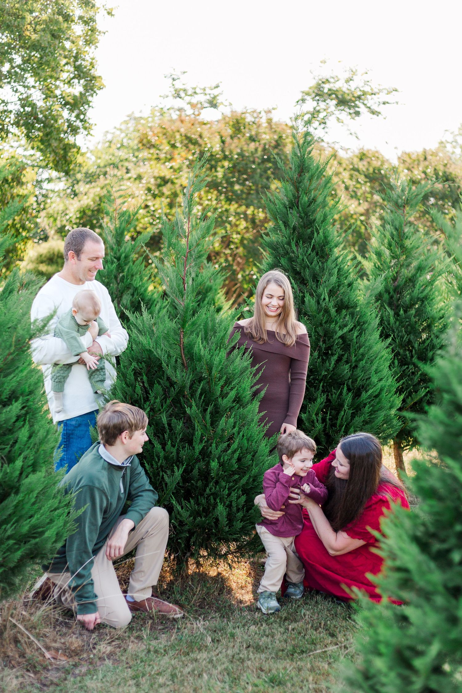 A family poses together among tall evergreen trees at a Christmas tree farm during the holiday season.