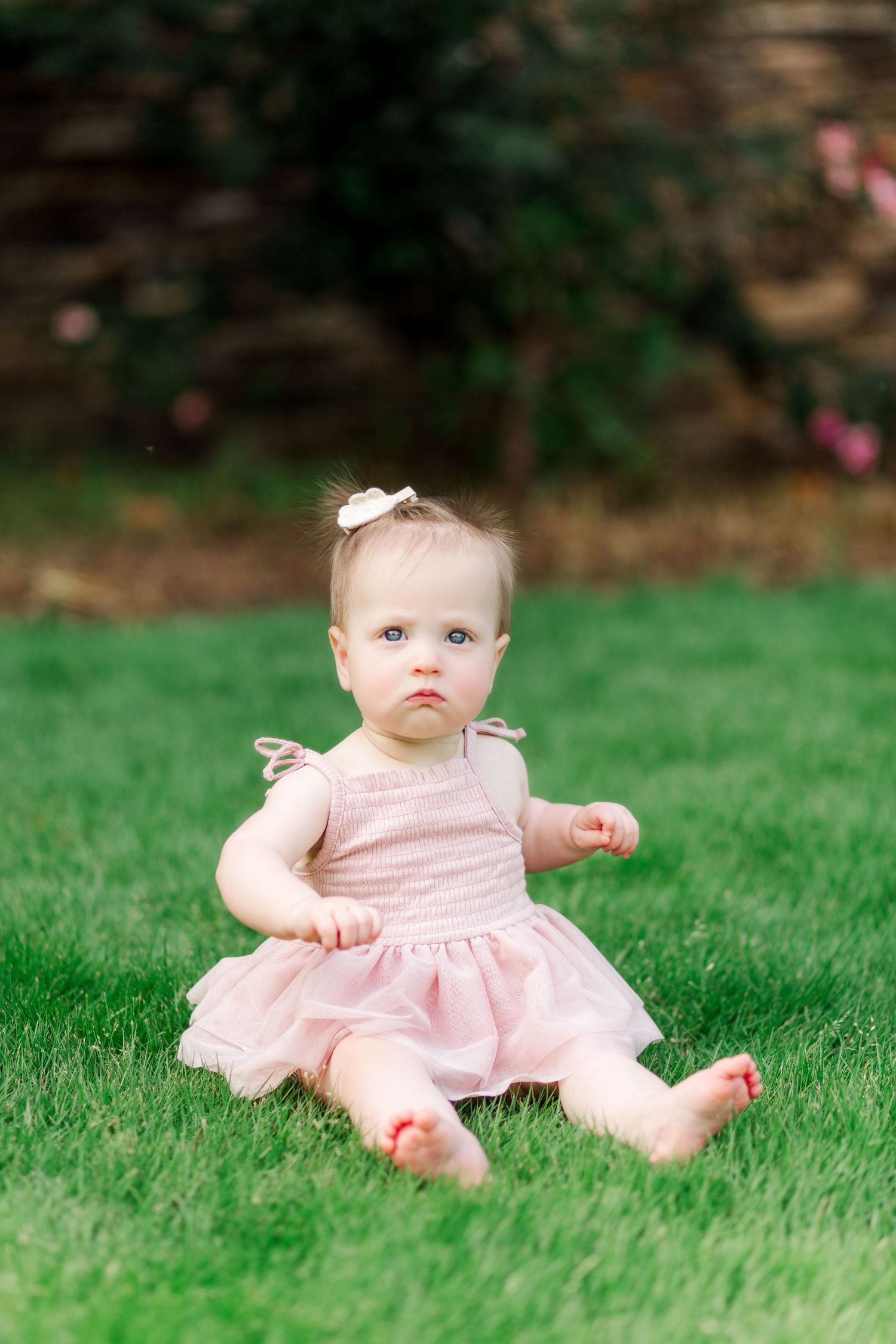 Baby in pink dress sitting on green grass in Clemson, Sc with a sweet expression for family photos.