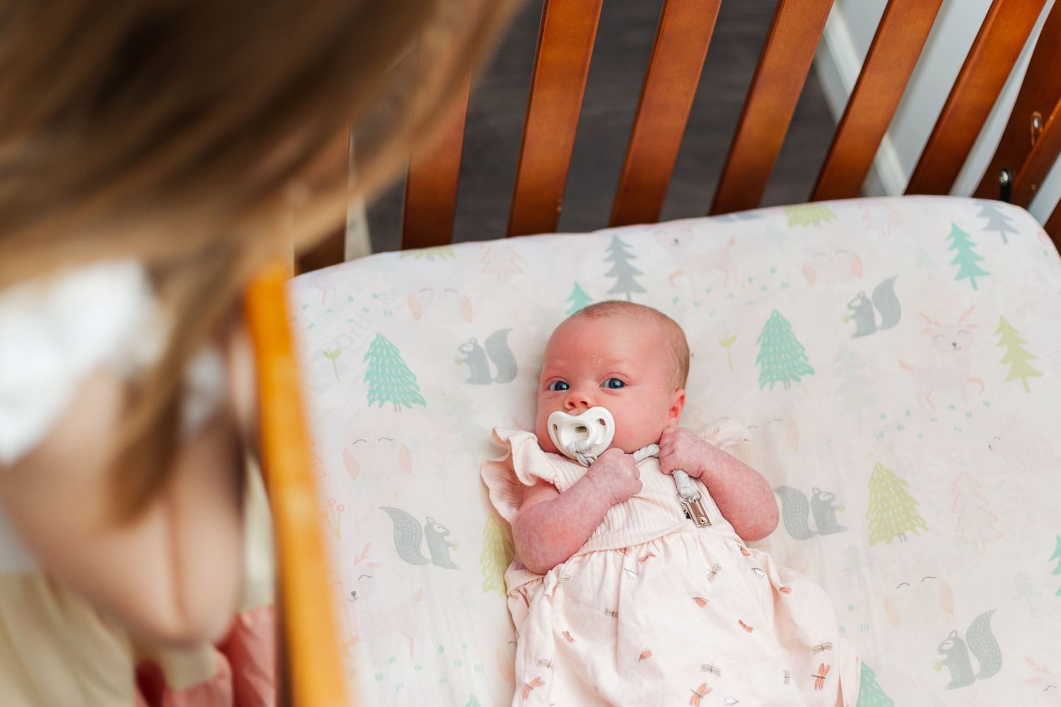 Young baby wrapped in a blanket with pine tree pattern resting on a wooden surface.