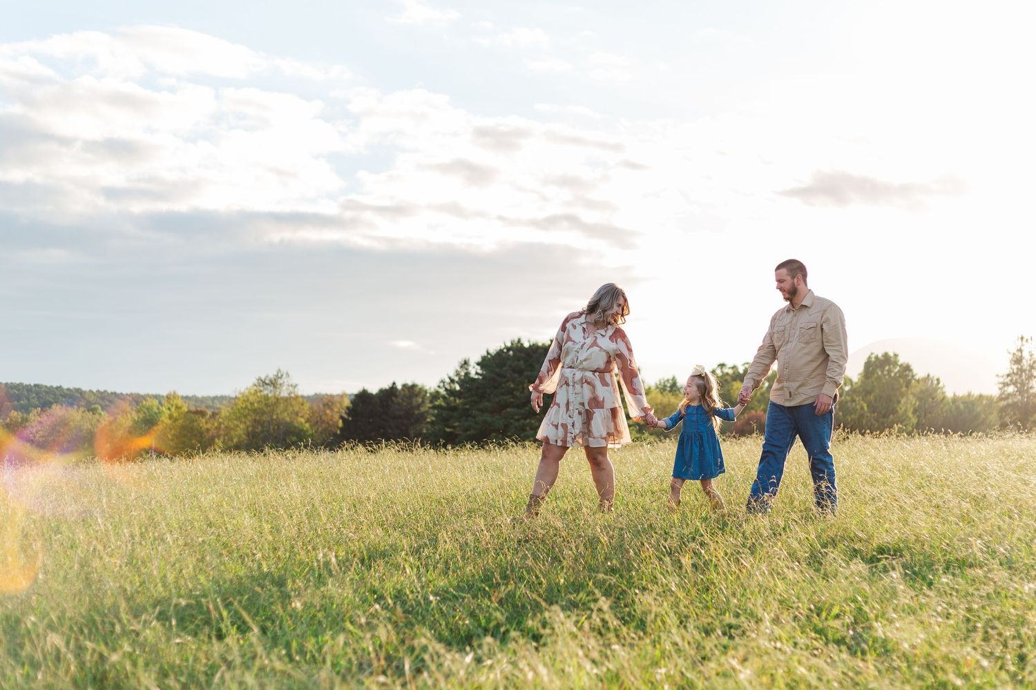 A wide landscape shot of a family walking through a golden field at dusk in Hendersonville, NC.